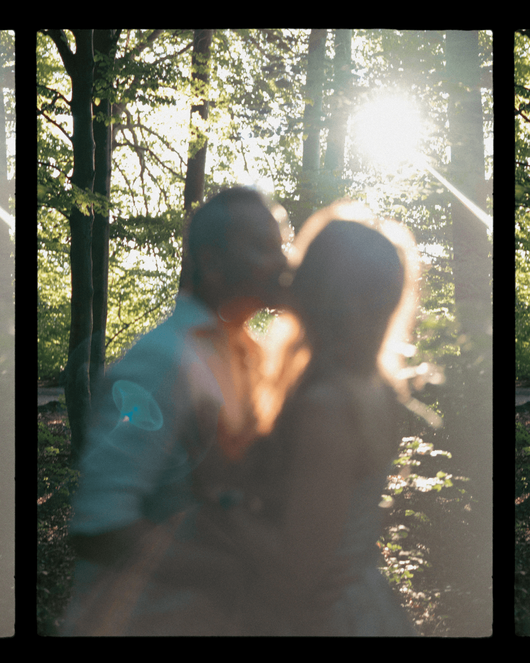 Couple sharing a kiss backlit by golden sunlight streaming through forest trees.