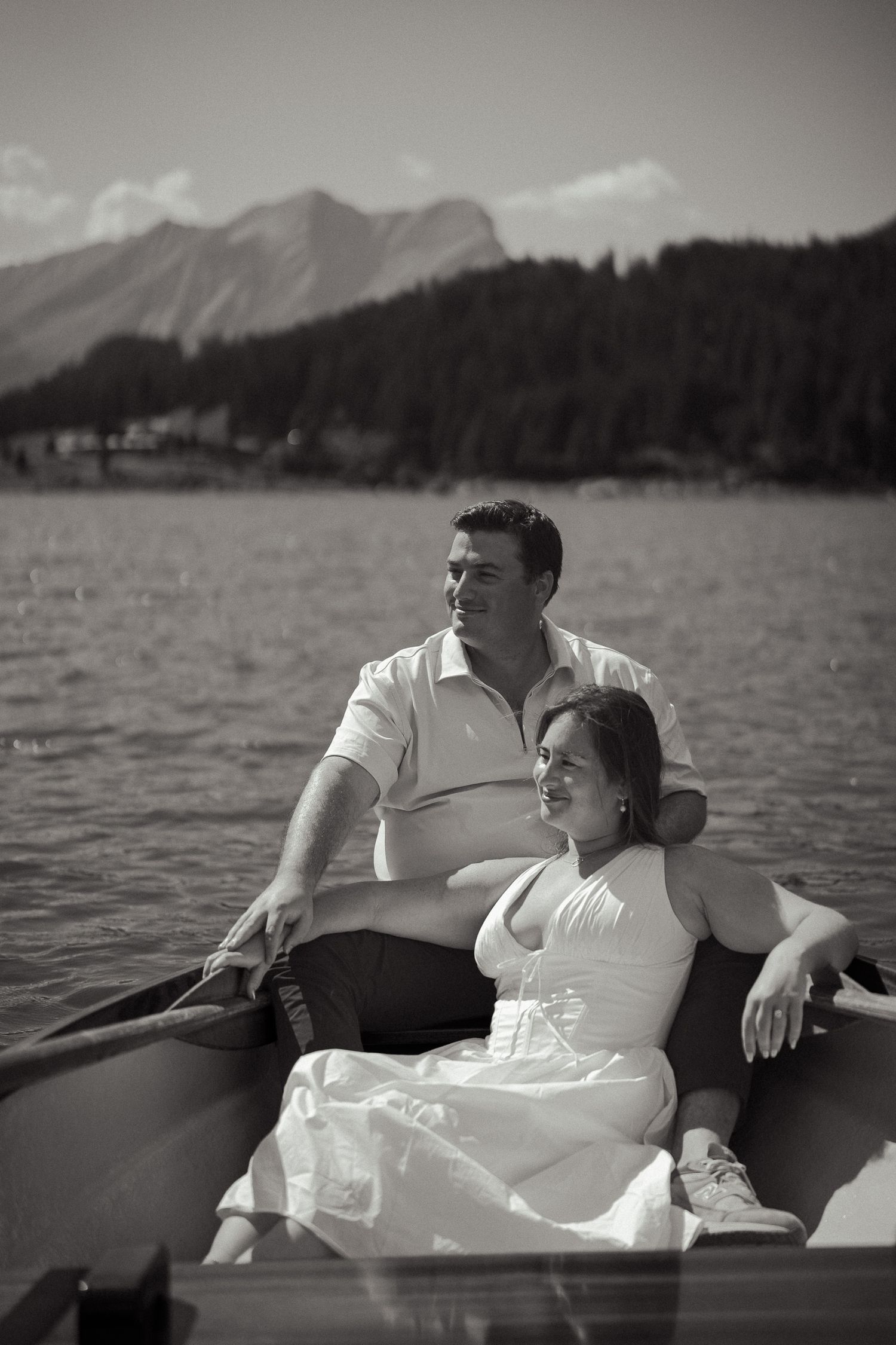 Couple relaxing in a rowboat on a mountain lake, black and white romantic photo with scenic alpine backdrop.