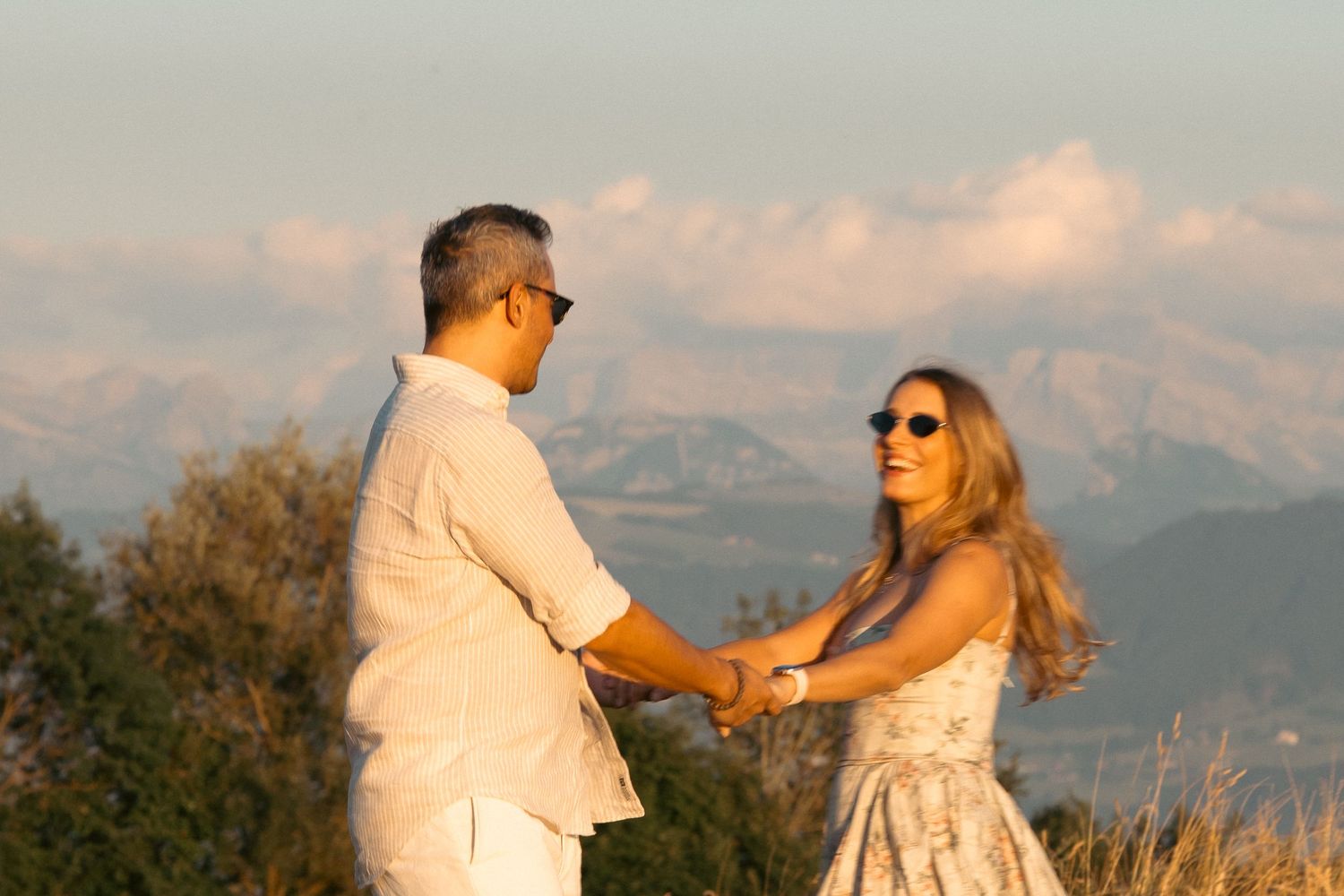 Couple holding hands at sunset with mountain backdrop during romantic outdoor engagement session.