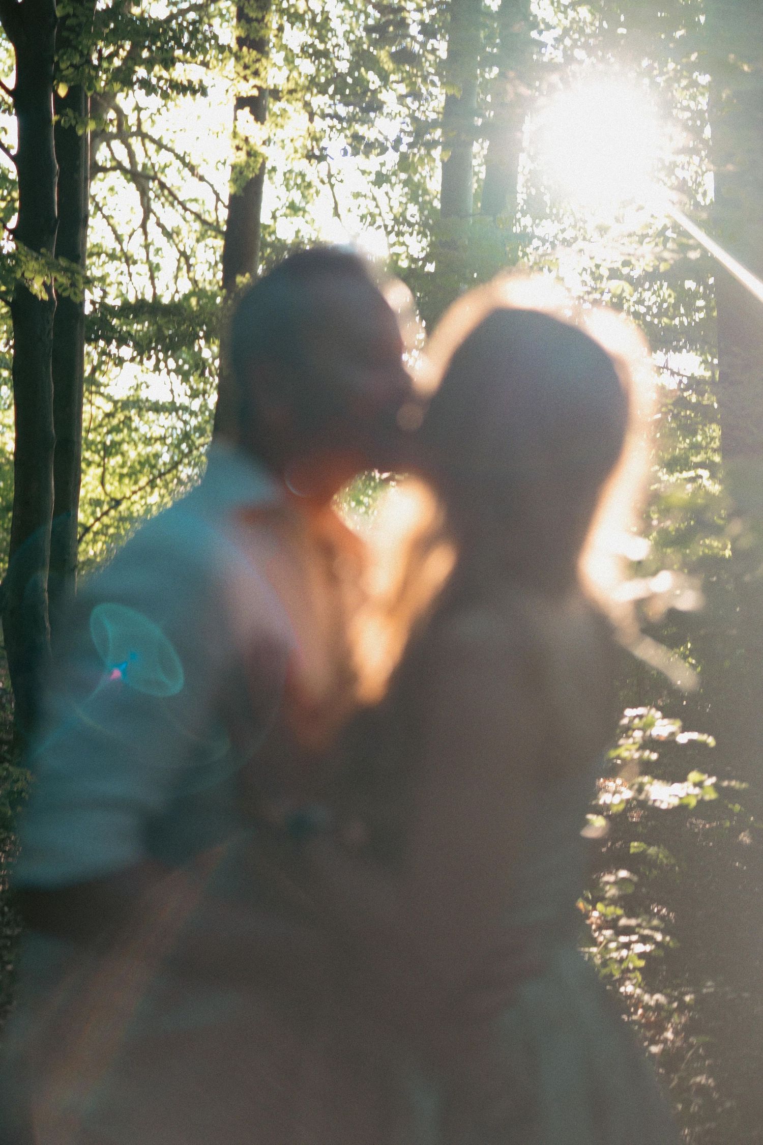 Couple sharing a romantic kiss in a sunlit forest with beautiful lens flare effect.