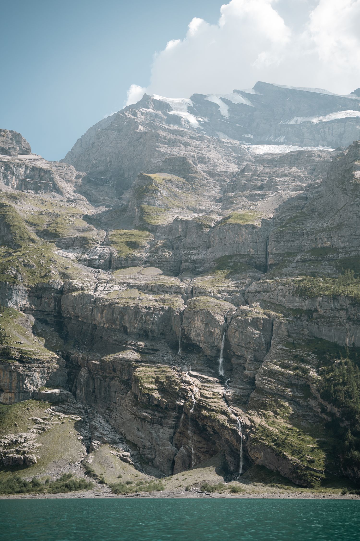 Dramatic alpine cliffs with cascading waterfalls above a turquoise mountain lake.
