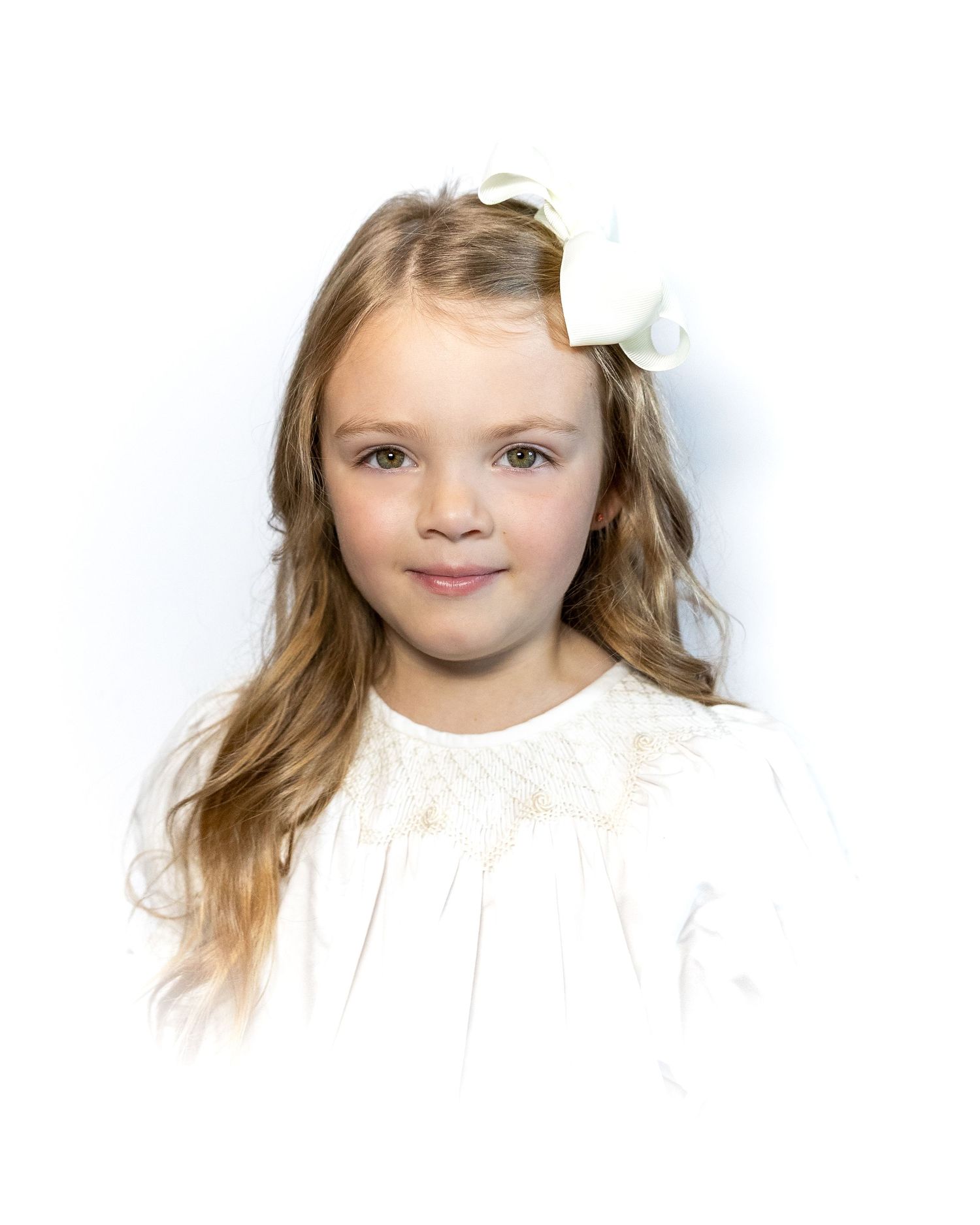 Young girl with long blonde hair wearing a white dress with a white bow hair accessory.