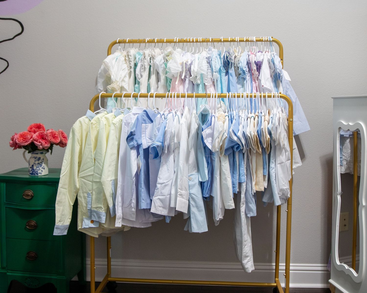 Gold clothing rack displaying pastel children's garments in blue, yellow, and white hues.