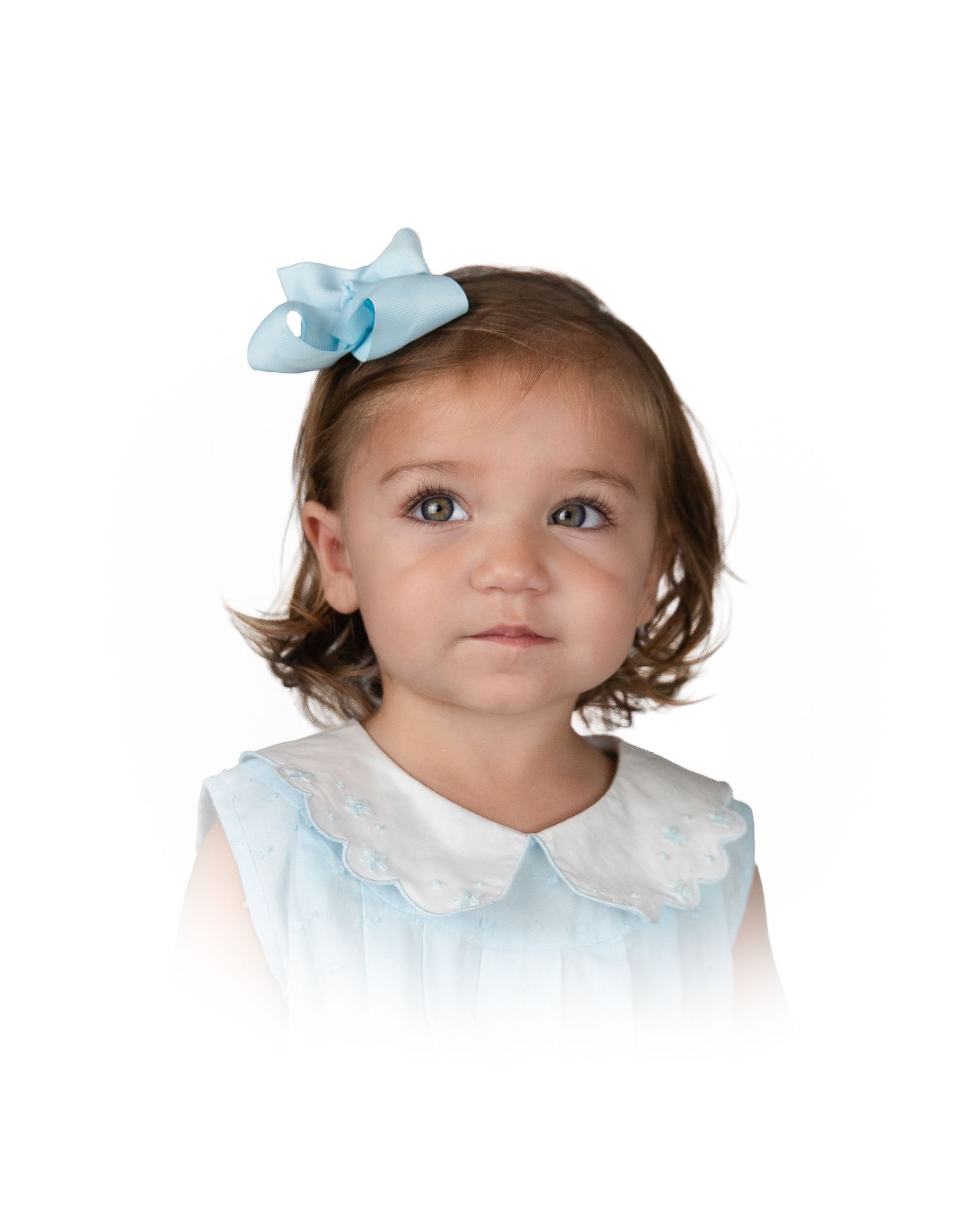 Baby girl with short brown hair wearing a blue bow clip and light blue lace collar dress.