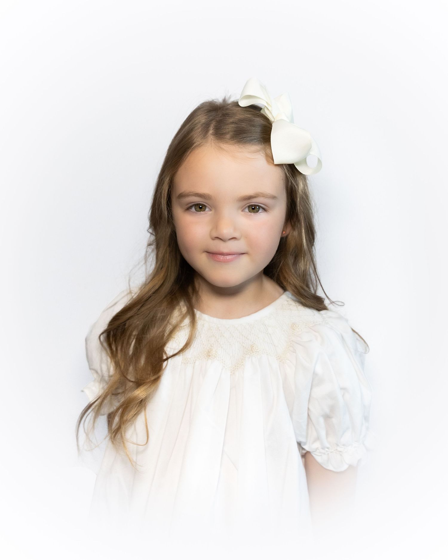 Young girl with long blonde hair wearing a white bow and white dress.