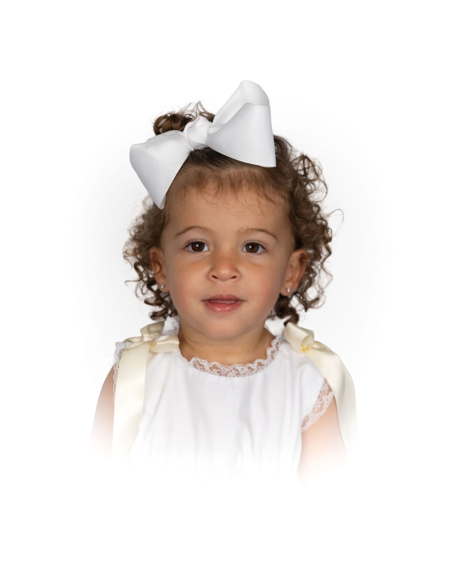 Smiling toddler girl with curly hair wearing a white bow hair clip.