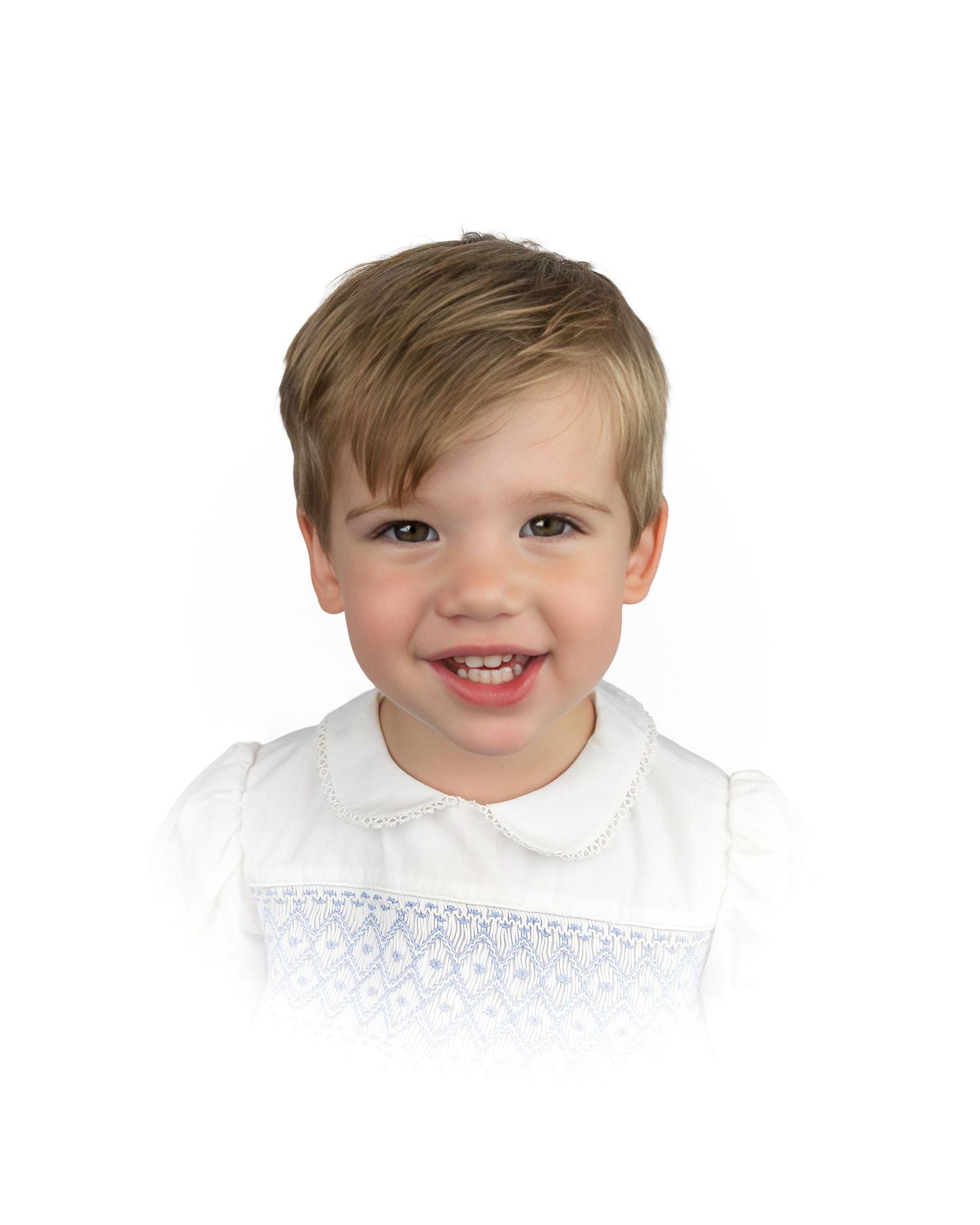 Toddler boy smiling in a white smocked dress with Peter Pan collar.
