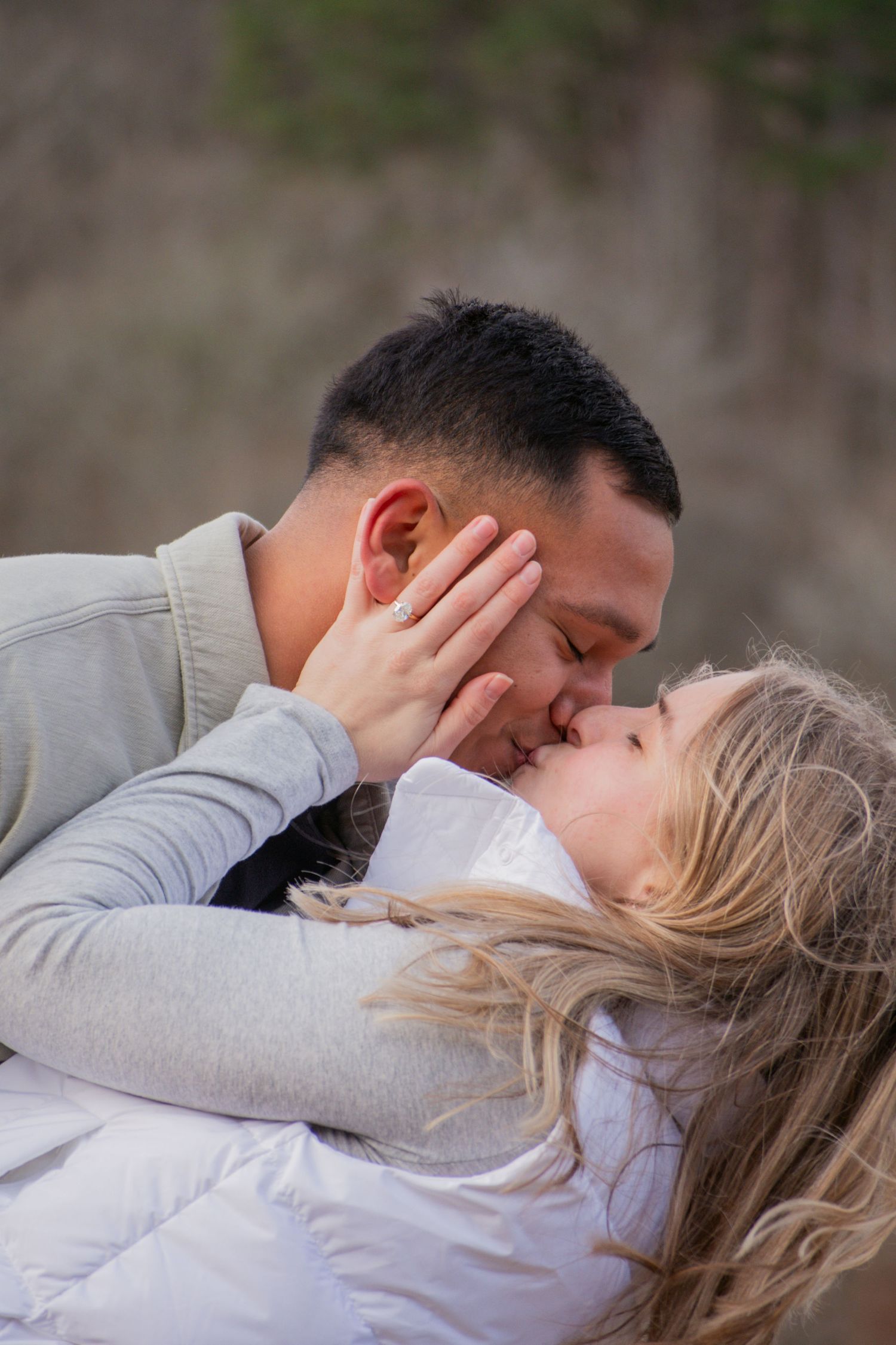 A couple shares a romantic kiss outdoors, with the woman tenderly placing her hand on the mans face.