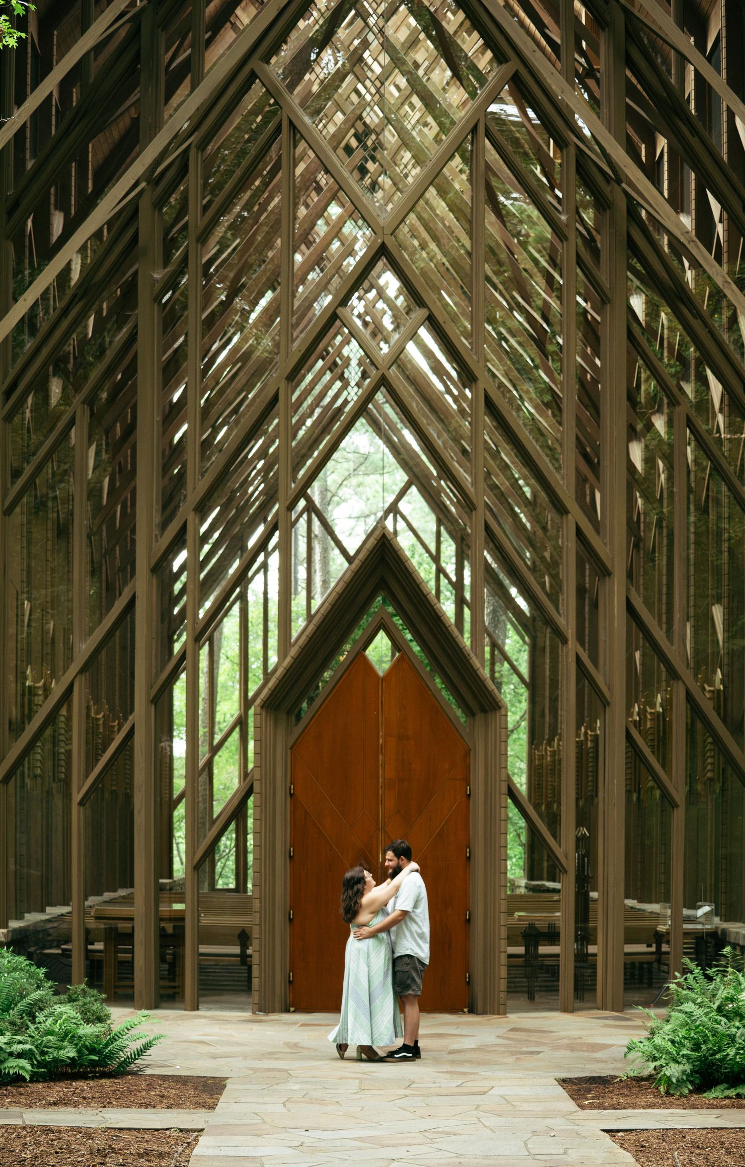 Couple embracing in a stunning open-air wooden chapel with soaring latticed arches and lush greenery.