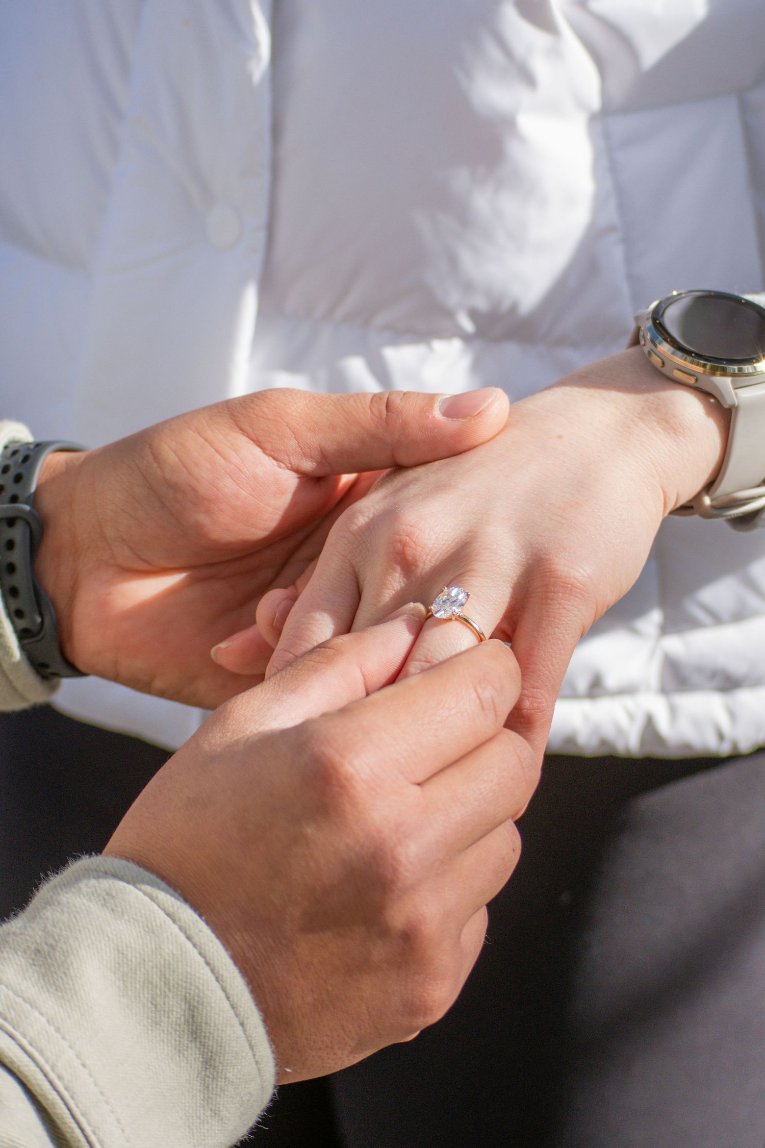 Close-up of groom placing diamond engagement ring on bride's finger during outdoor proposal.