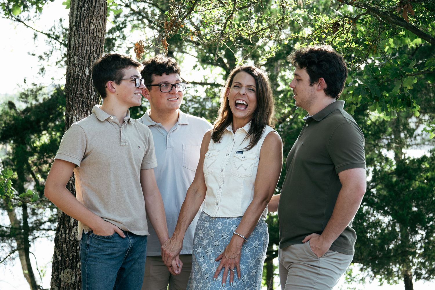 Four people laughing together outdoors among green trees during a casual family portrait session.