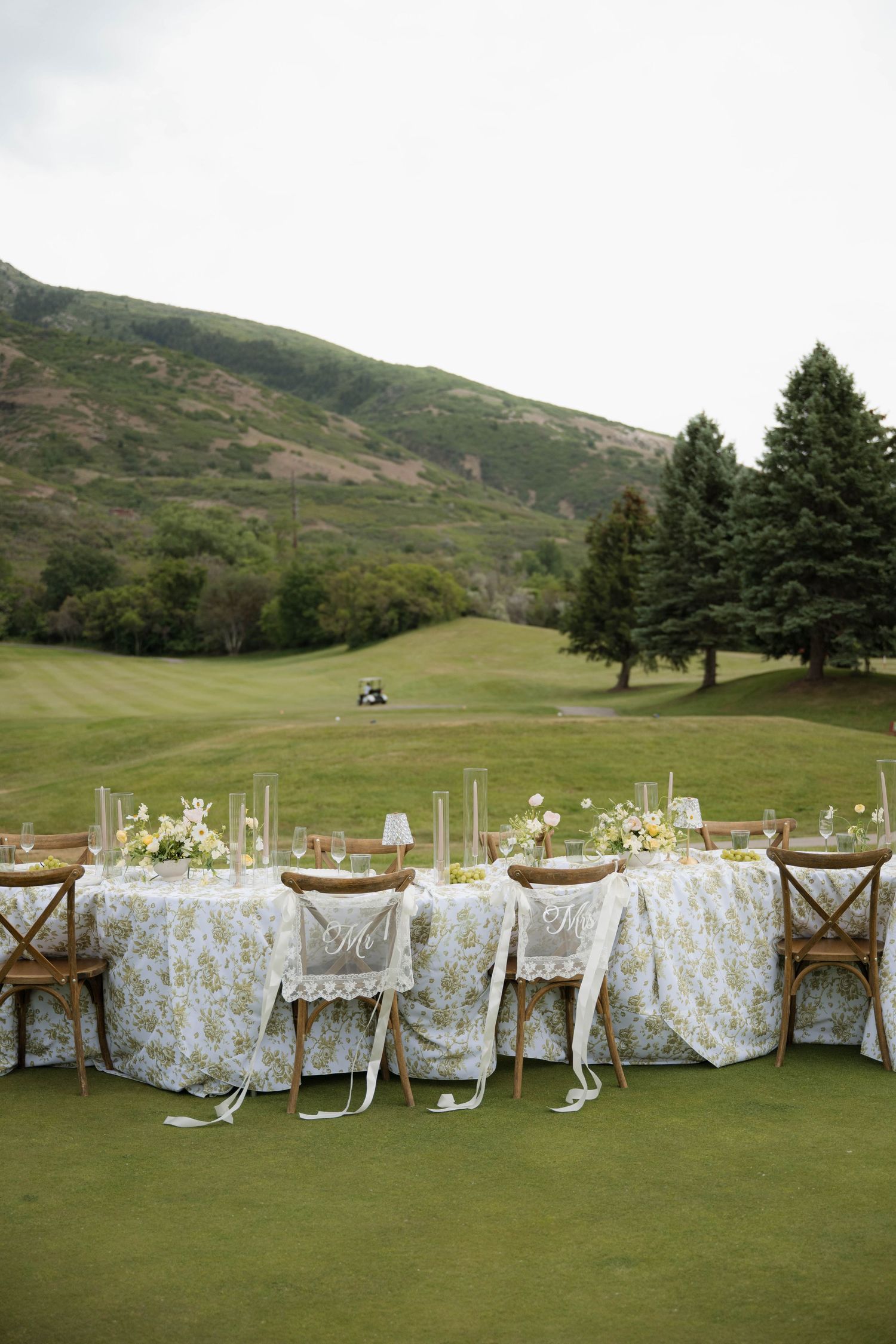 Wedding sweetheart table with Mr. and Mrs. chairs on lush golf course with mountain scenery.