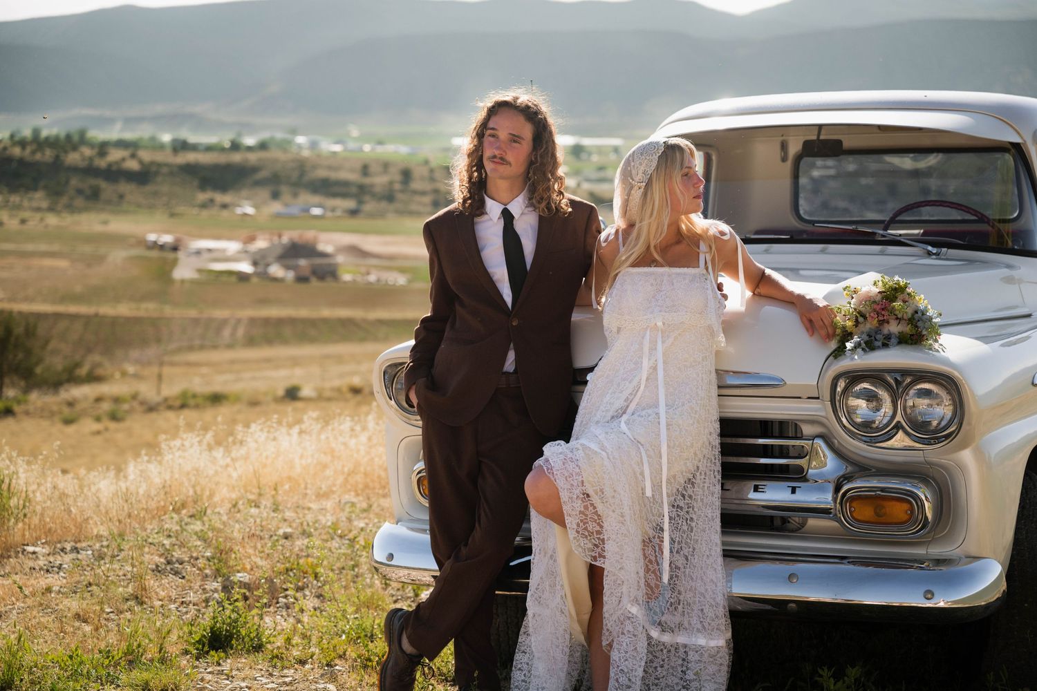 Bride and groom posing beside a vintage cream Chevrolet truck in a scenic mountain valley landscape.