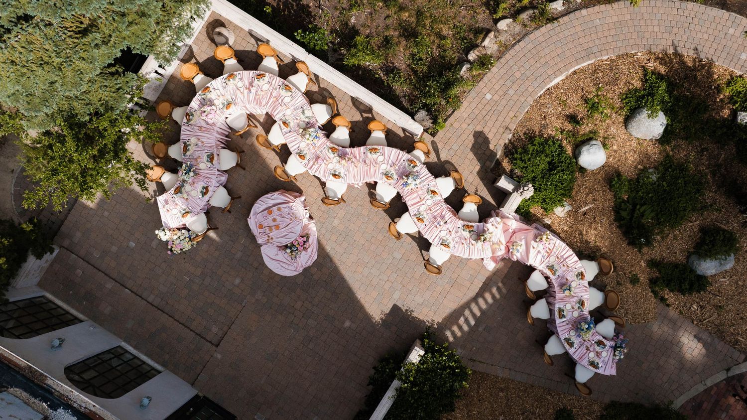 Aerial view of an elegantly decorated outdoor wedding reception with long floral tables and white chairs.