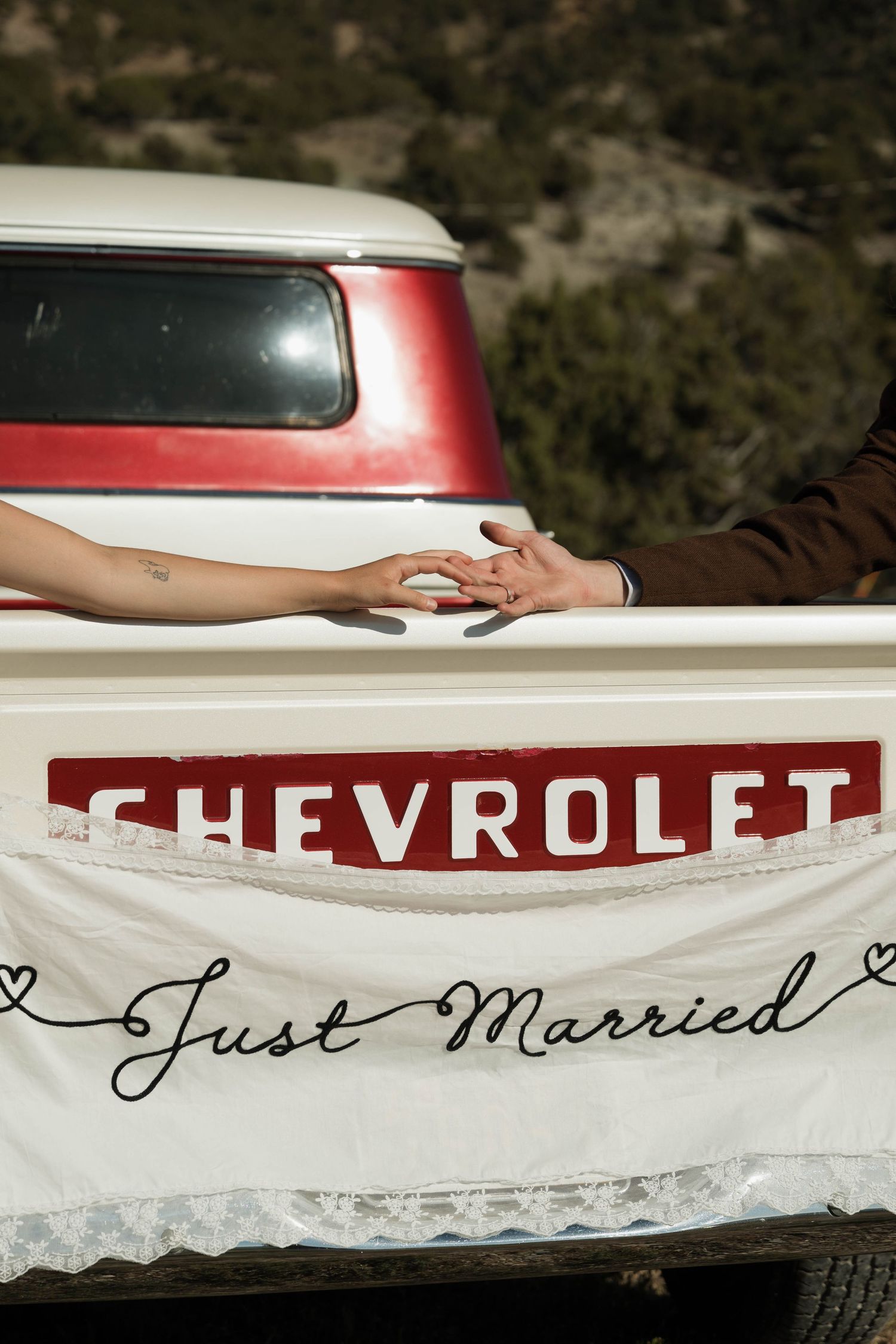 Newlywed couple holding hands over a Just Married banner on a vintage Chevrolet truck tailgate.