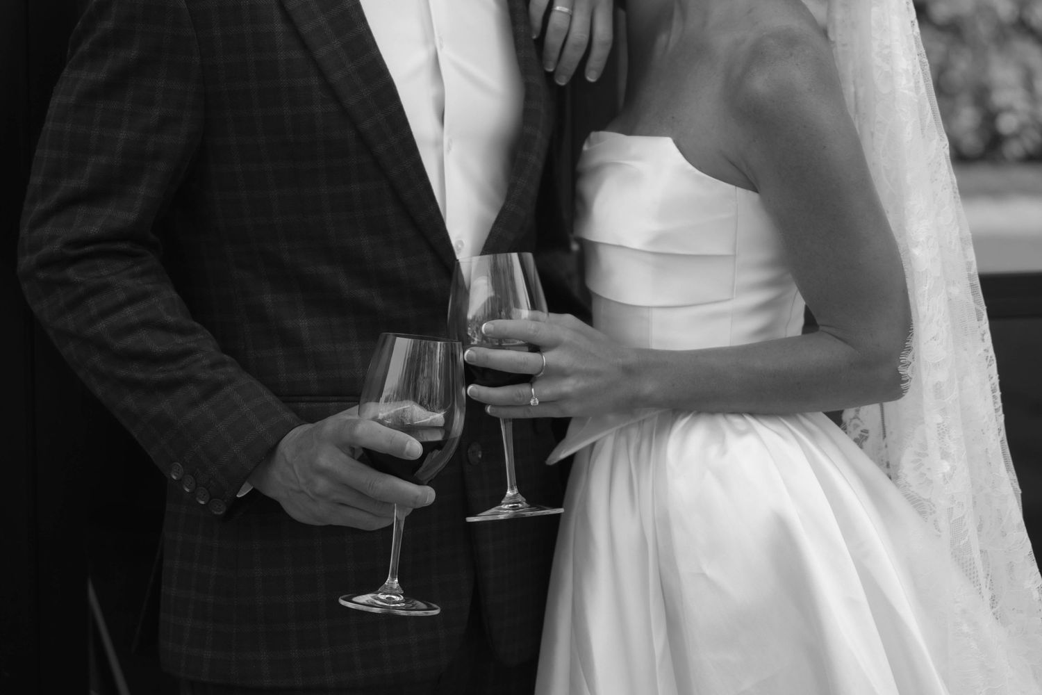 Black and white photo of a bride and groom holding wine glasses at their wedding reception.