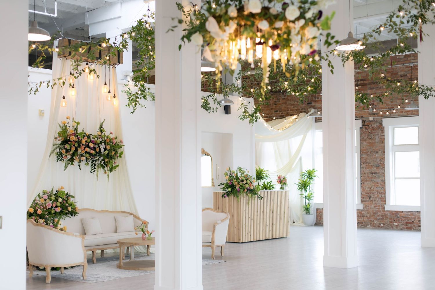 Elegant wedding venue with white columns, floral chandeliers, and greenery decorations.