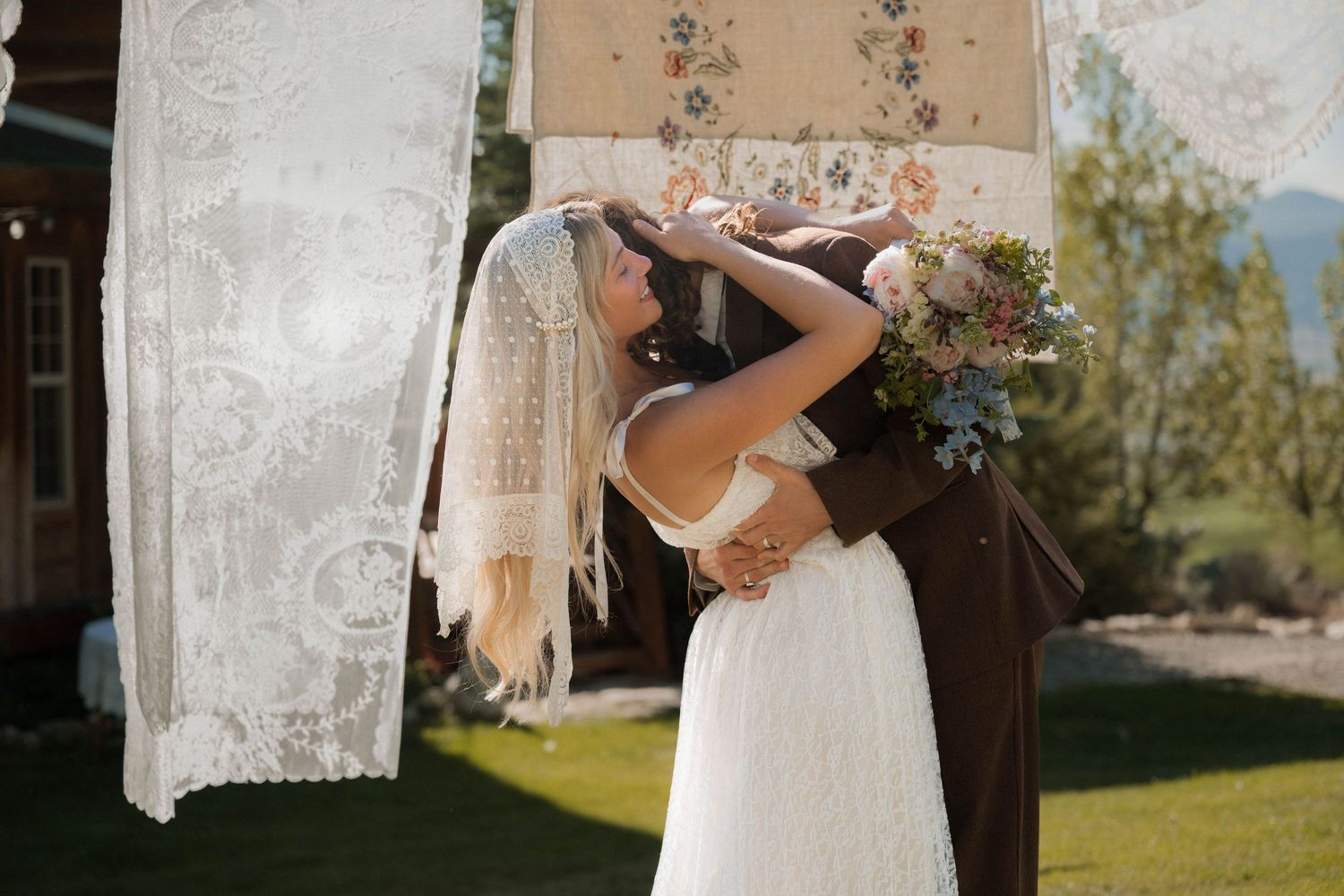Bride and groom sharing a romantic kiss in front of decorative hanging vintage lace linens at outdoor wedding.