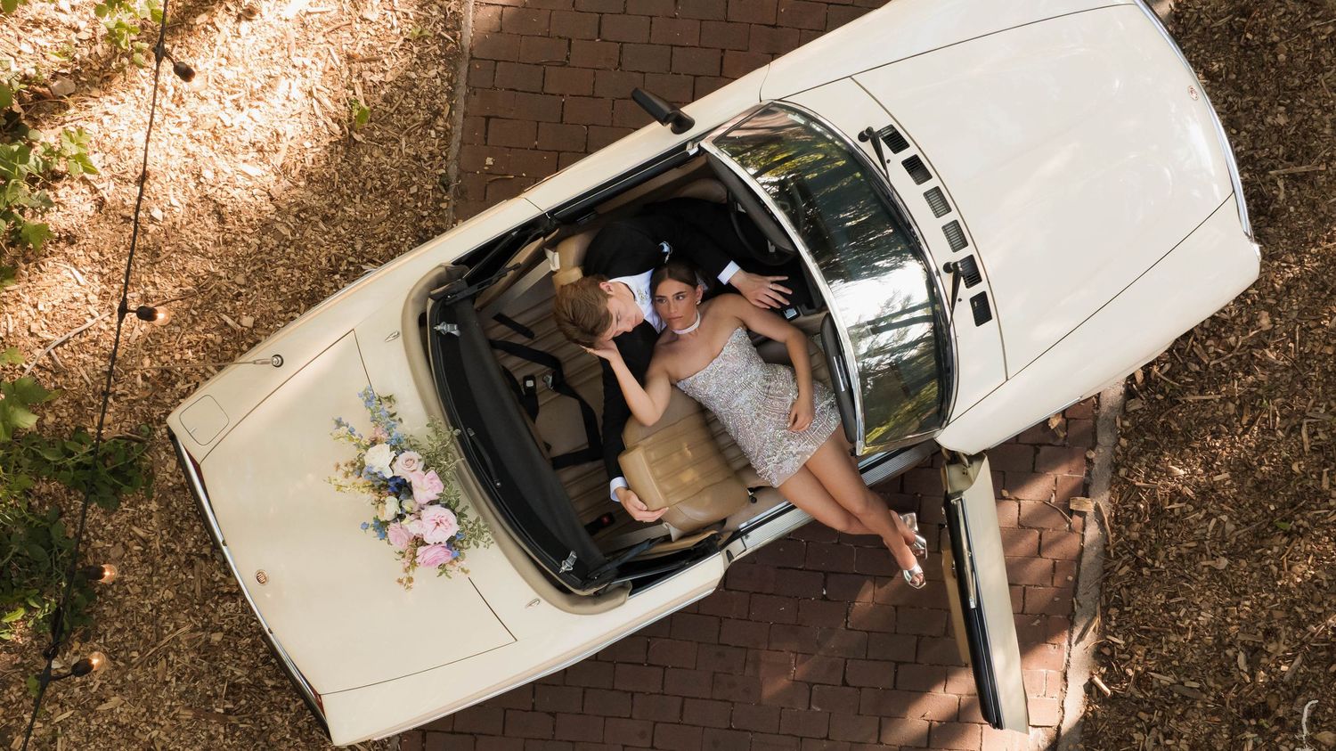 Aerial view of a bride posing beside a white vintage convertible decorated with floral arrangements.