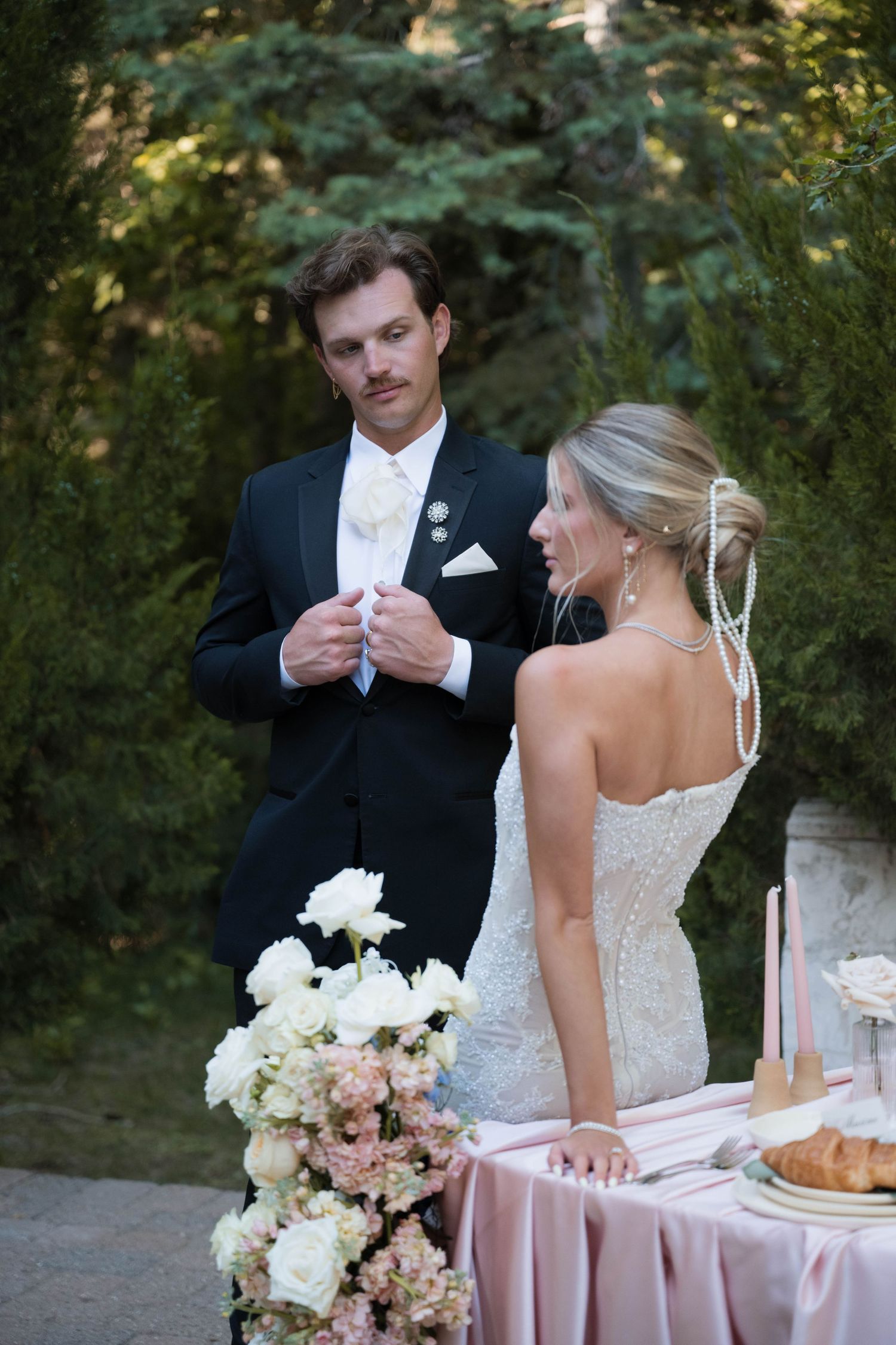 Bride and groom share a glance beside a floral centerpiece at an outdoor wedding reception table.