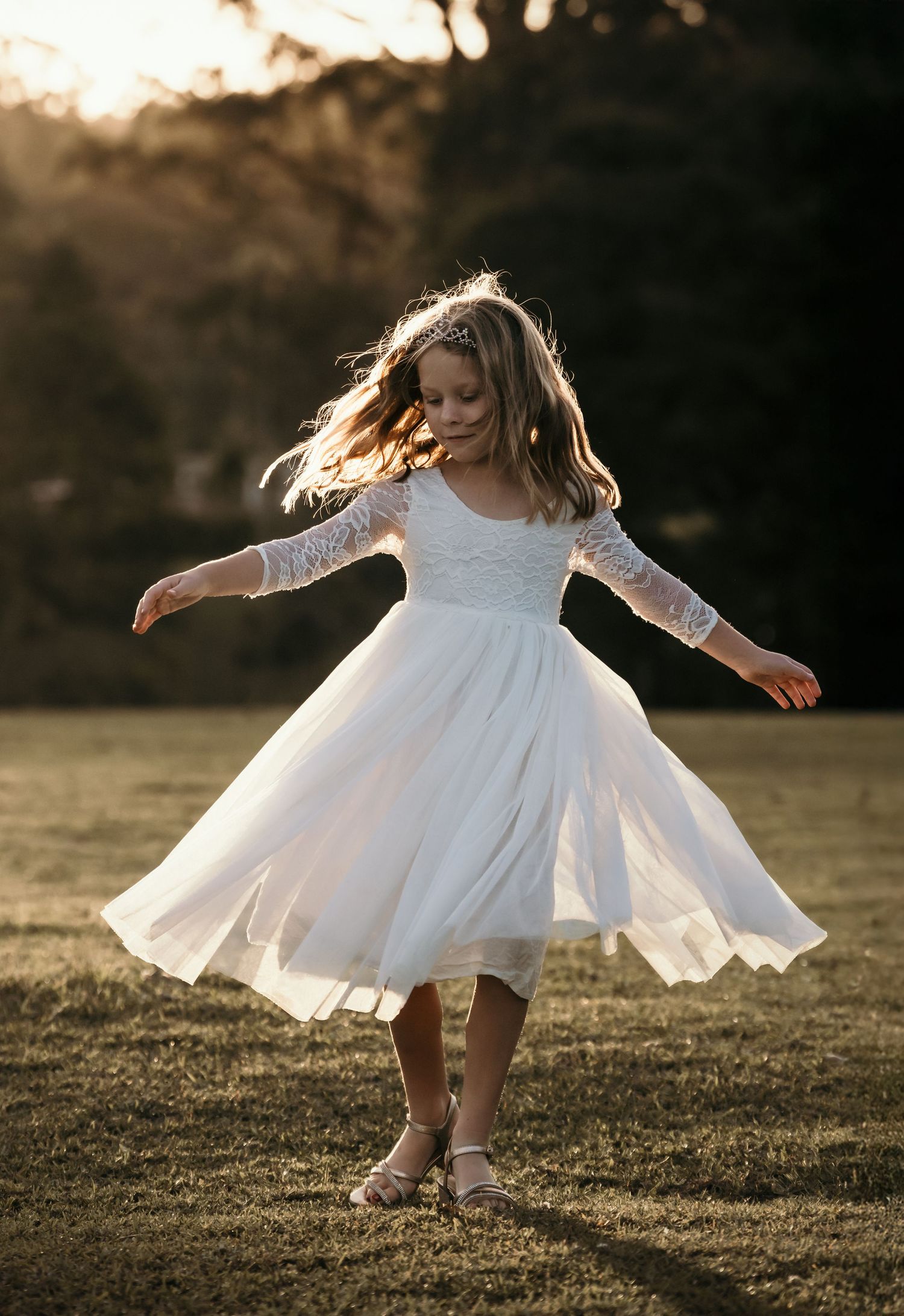 A young girl in a white lace dress twirls joyfully in a sunlit field, her hair flowing in the golden light.