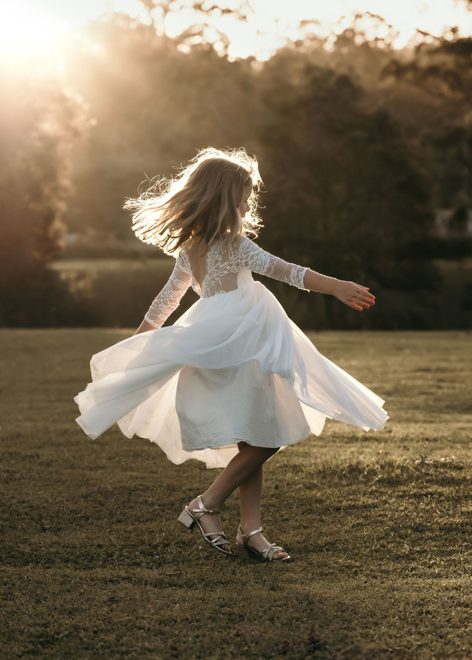 Young girl in white lace dress twirling in sunlit field at golden hour, hair flowing freely.