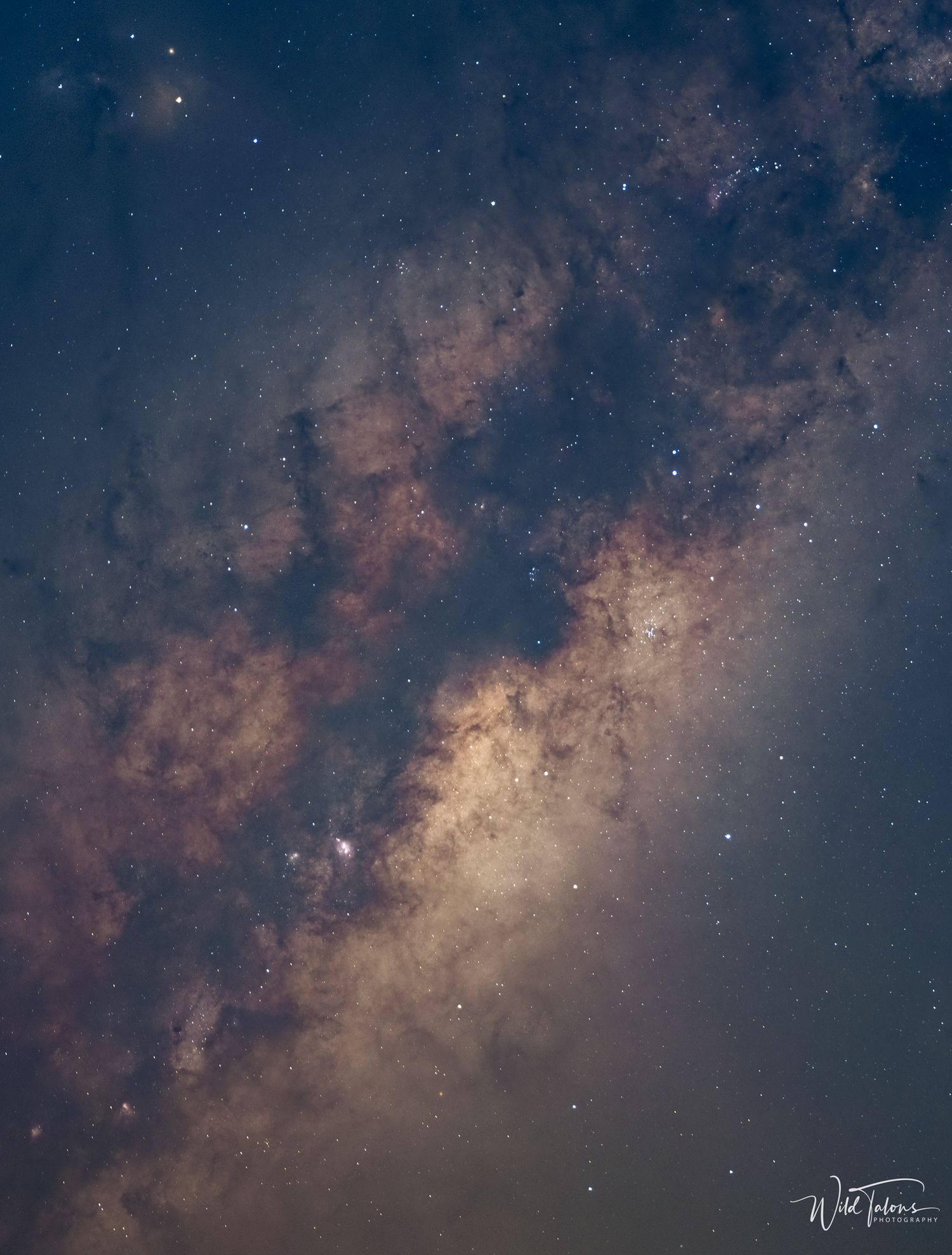 Stunning Milky Way galaxy core with dark nebulae and glowing star clouds photographed against a deep blue night sky.