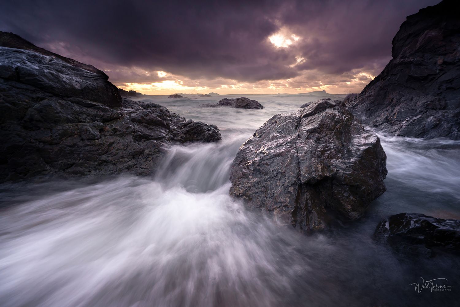 Dramatic seascape with crashing waves over rocky shore under stormy purple sky at sunset.