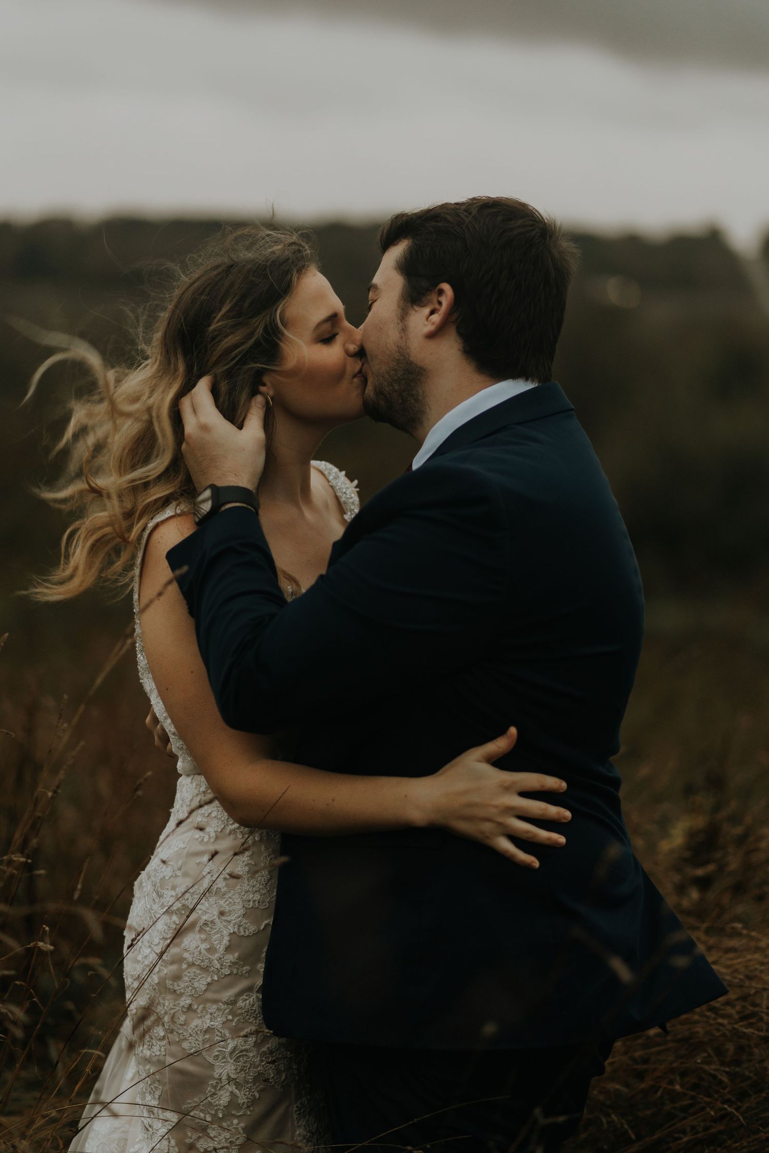Bride and groom sharing a romantic kiss in a moody outdoor field on their wedding day.
