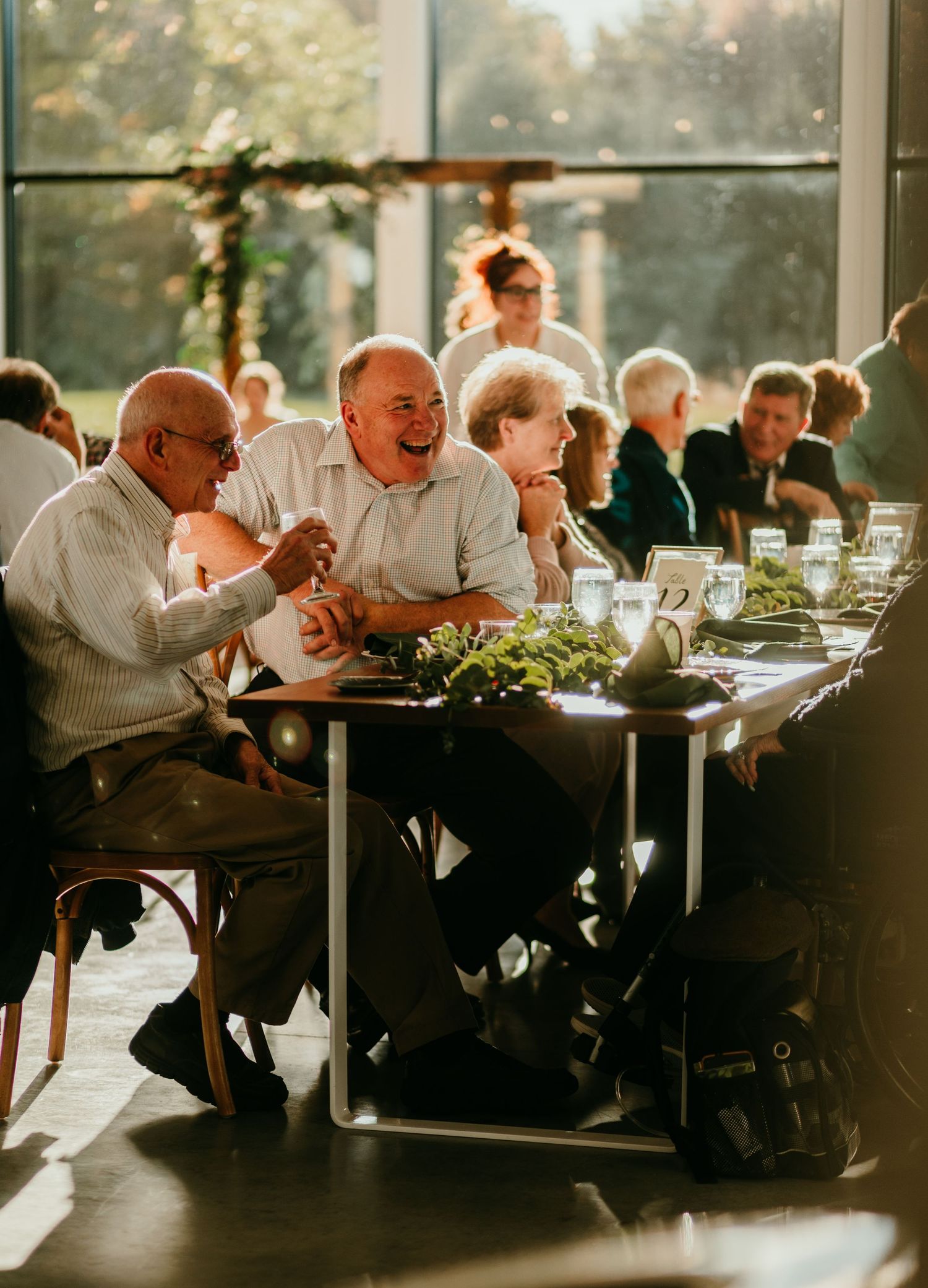 Guests laughing and socializing at an elegant indoor reception with greenery table centerpieces.