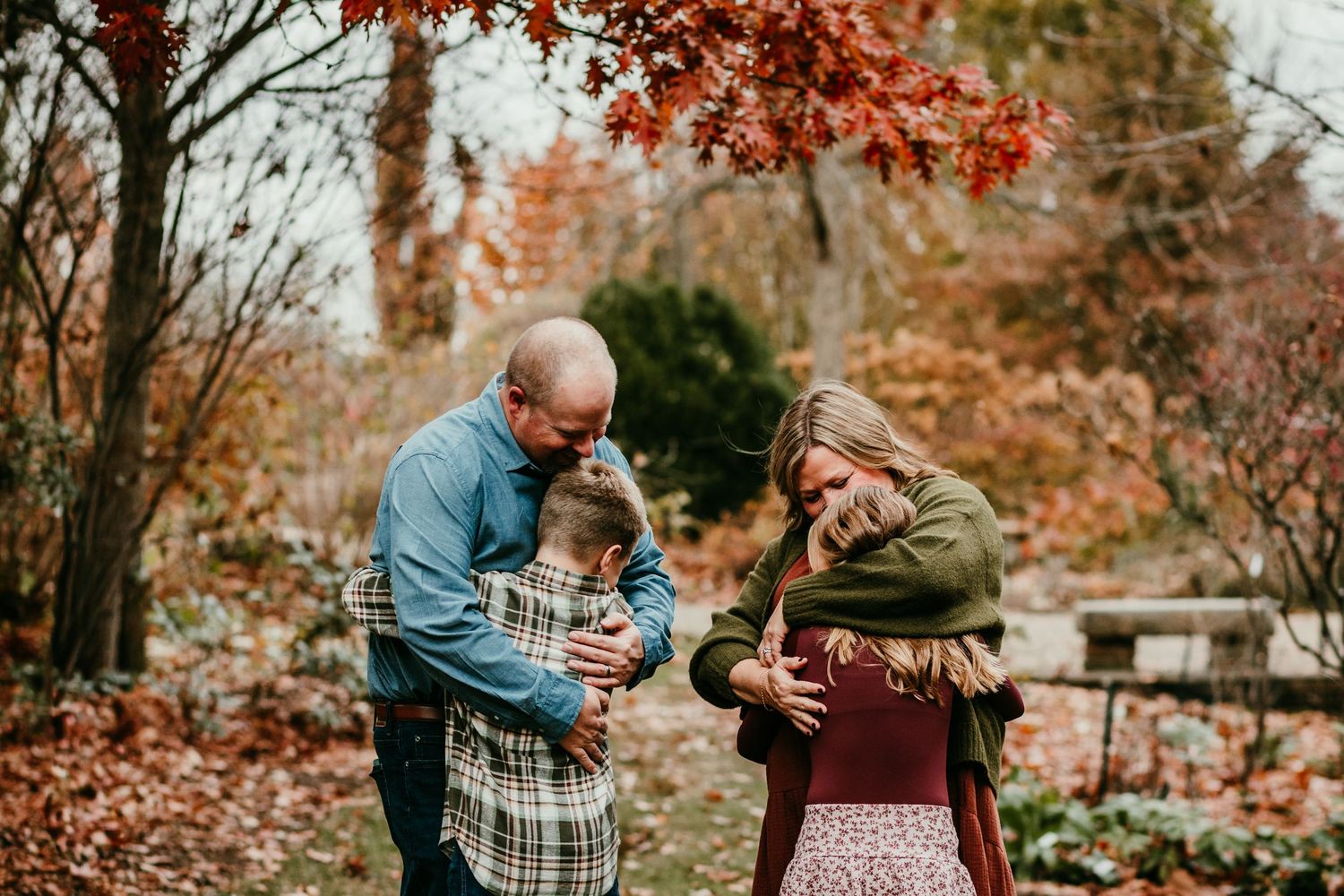Family of four sharing a tender embrace in an autumn garden with colorful fall foliage.