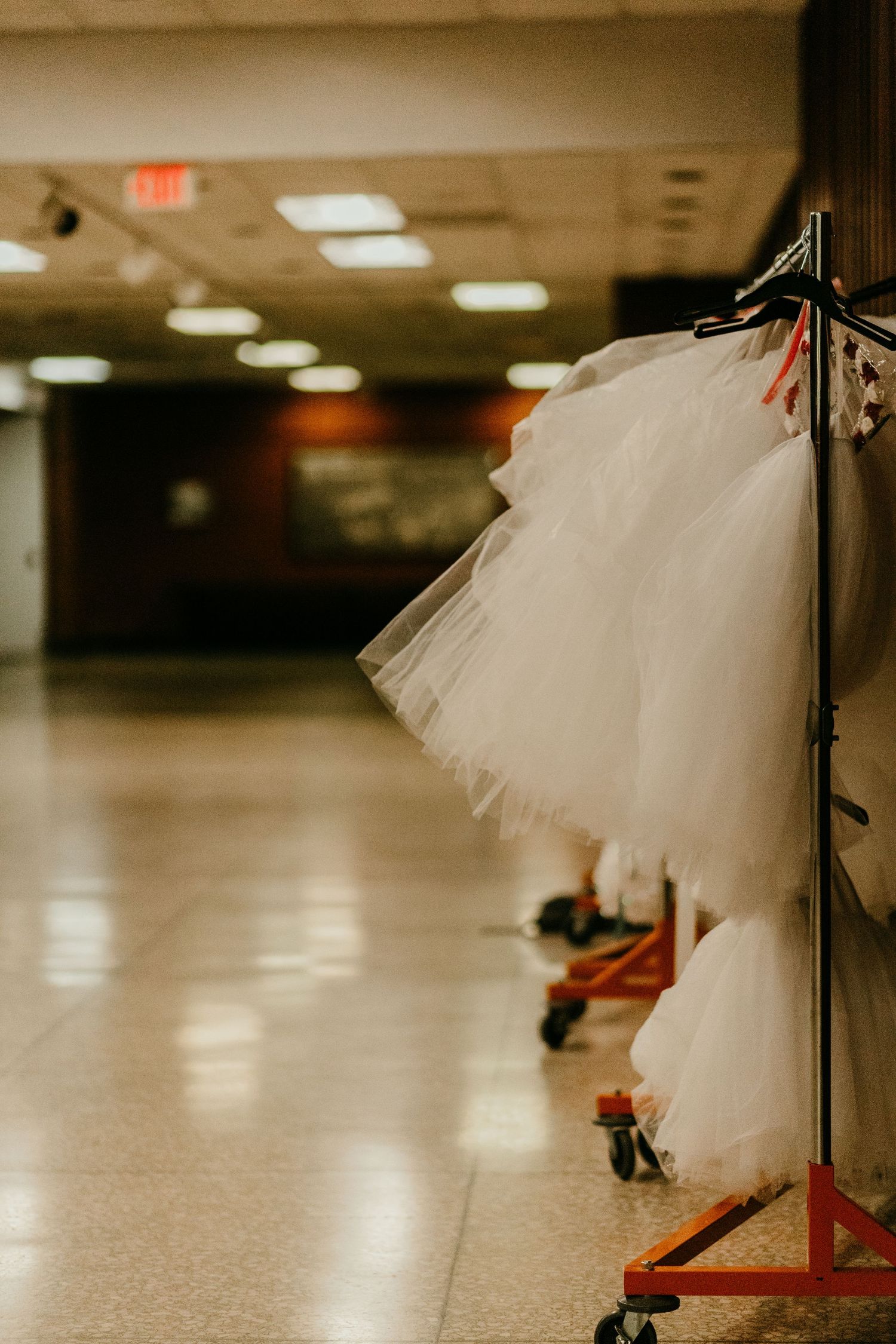 White tutu ballet costumes hanging on a rolling rack in a backstage hallway.
