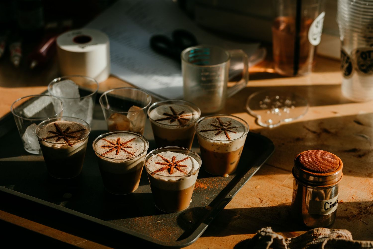 Tray of decorated latte art coffee cups in warm golden sunlight on a wooden surface.