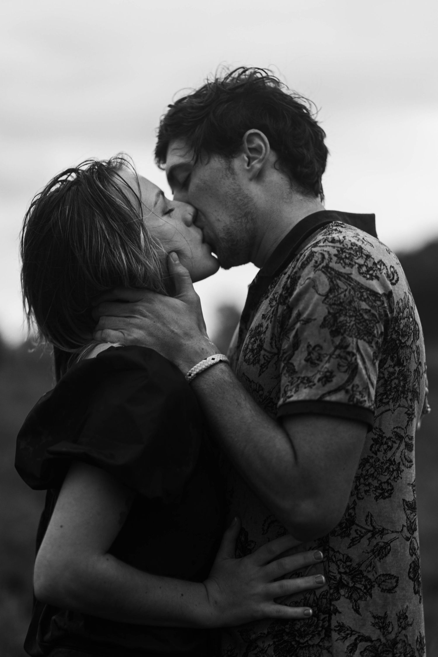 Black and white close-up of passionate couple kissing outdoors in moody lighting.
