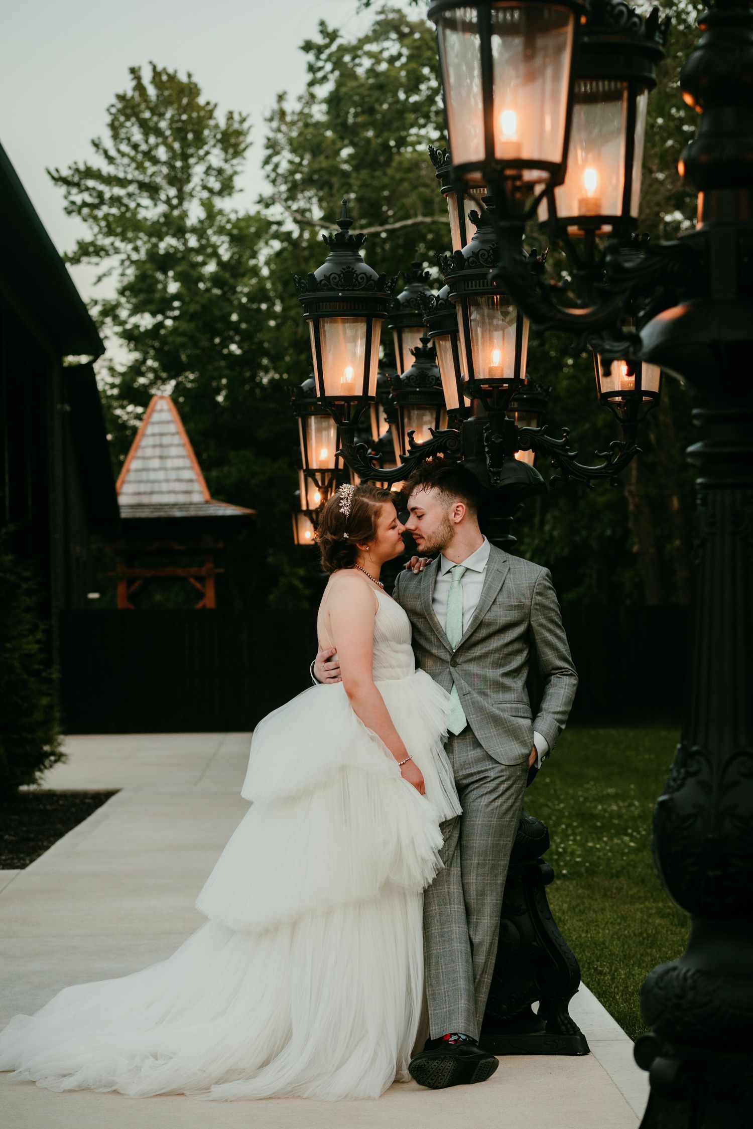 Bride and groom share a tender kiss beside vintage lanterns at dusk in a lush garden wedding setting.