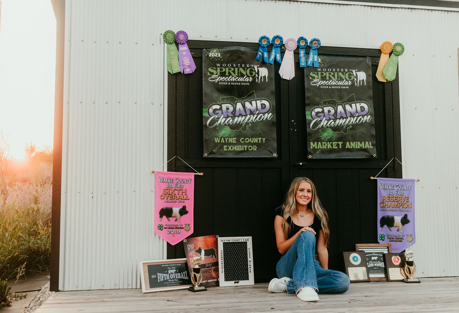 Young woman sitting before 4H banners with trophies and awards displayed.
