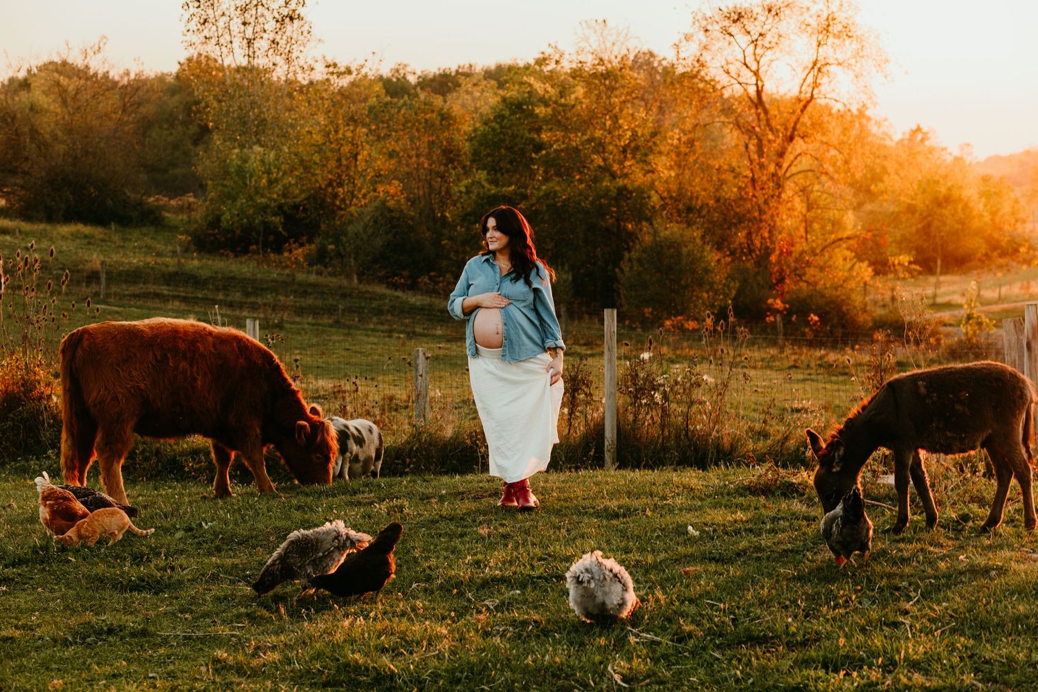 Pregnant woman in white skirt walking among farm animals including cattle and chickens at golden hour.