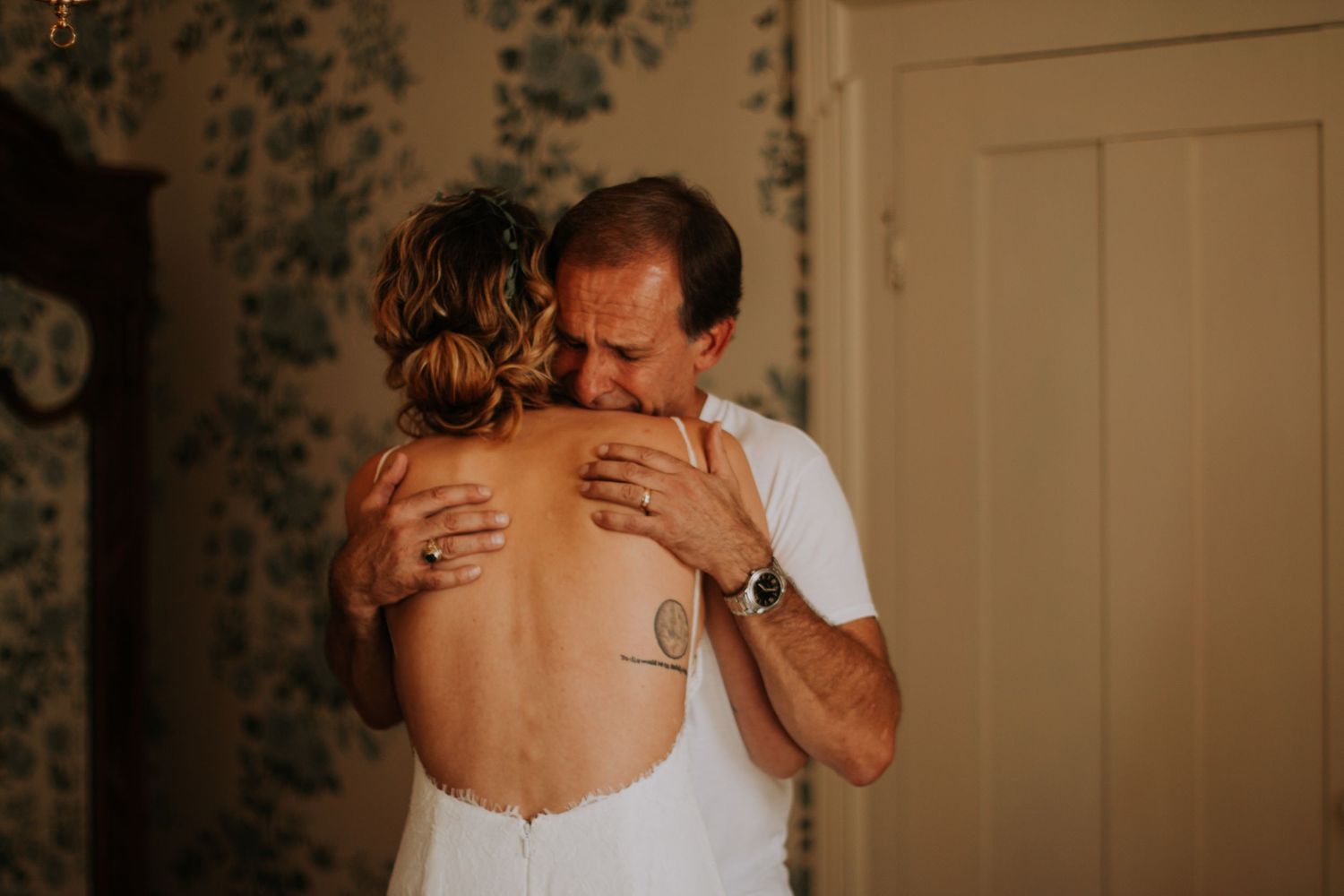 A father shares a heartfelt embrace with his bride daughter in her backless wedding gown before the ceremony.