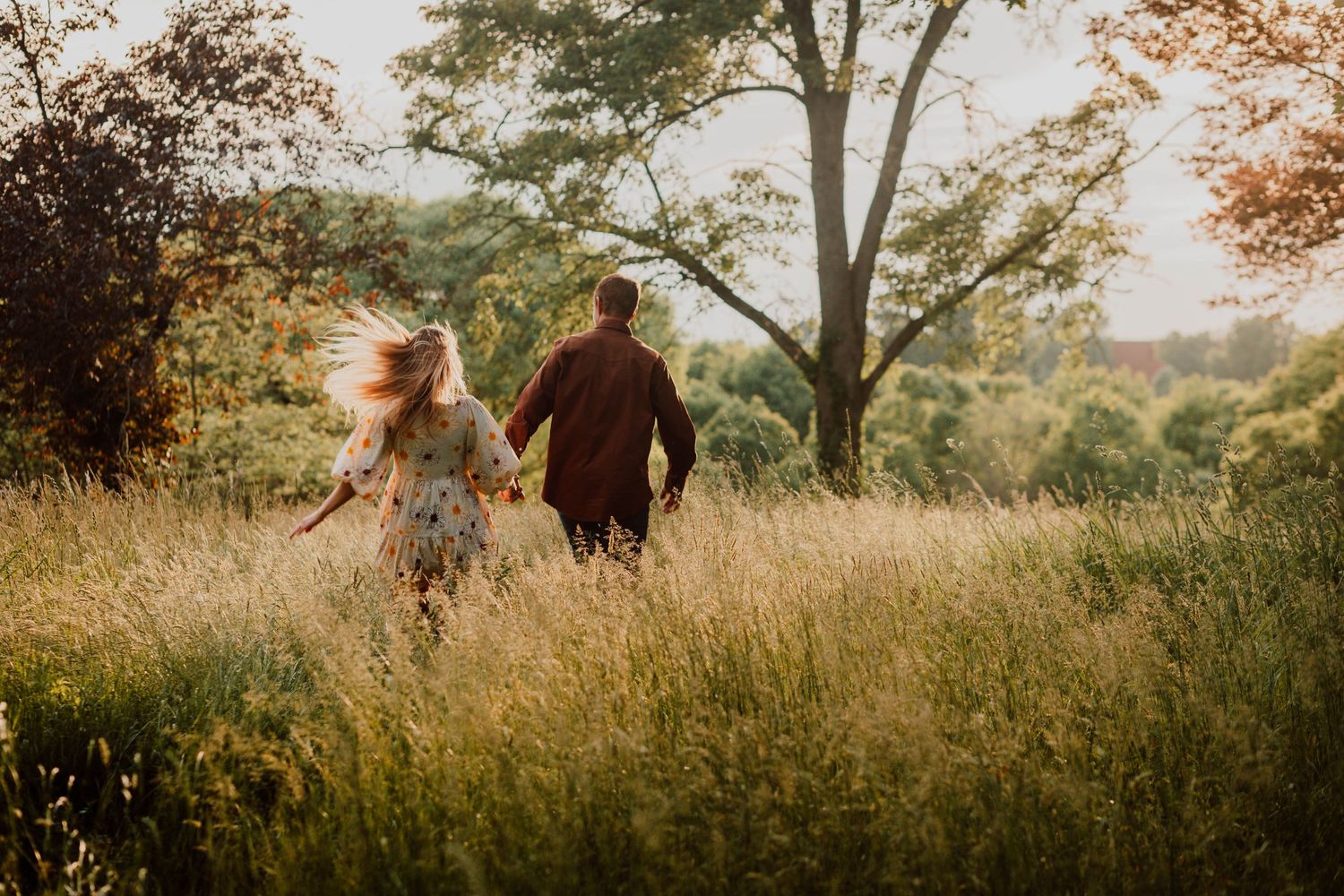 Couple holding hands running through golden tall grass meadow at sunset.