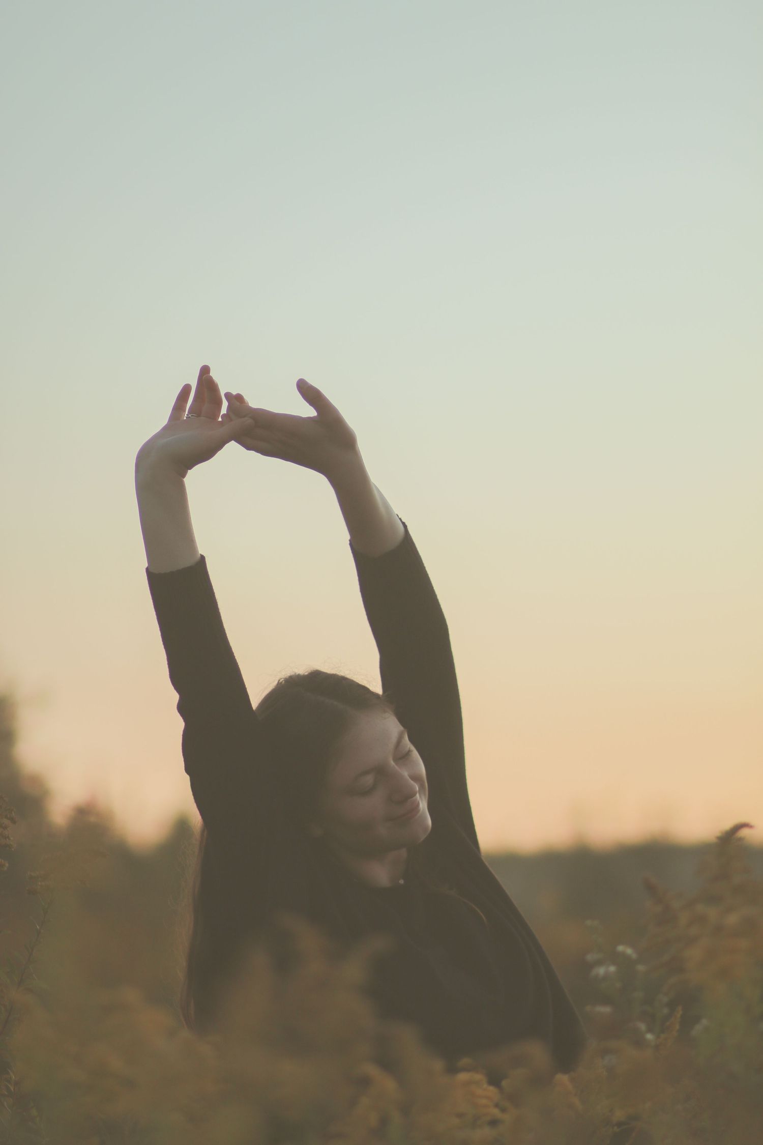 Young woman stretching arms overhead in a golden wildflower field at sunset.