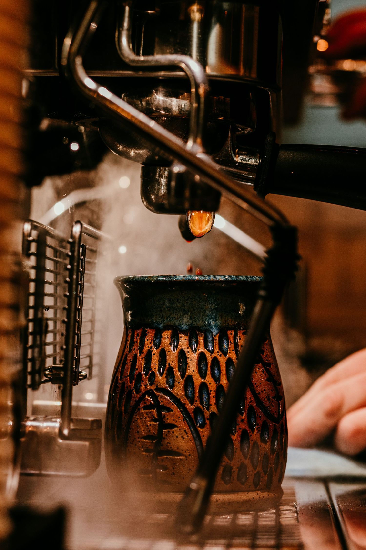 Espresso machine brewing coffee into a rustic handcrafted ceramic mug with steam rising.