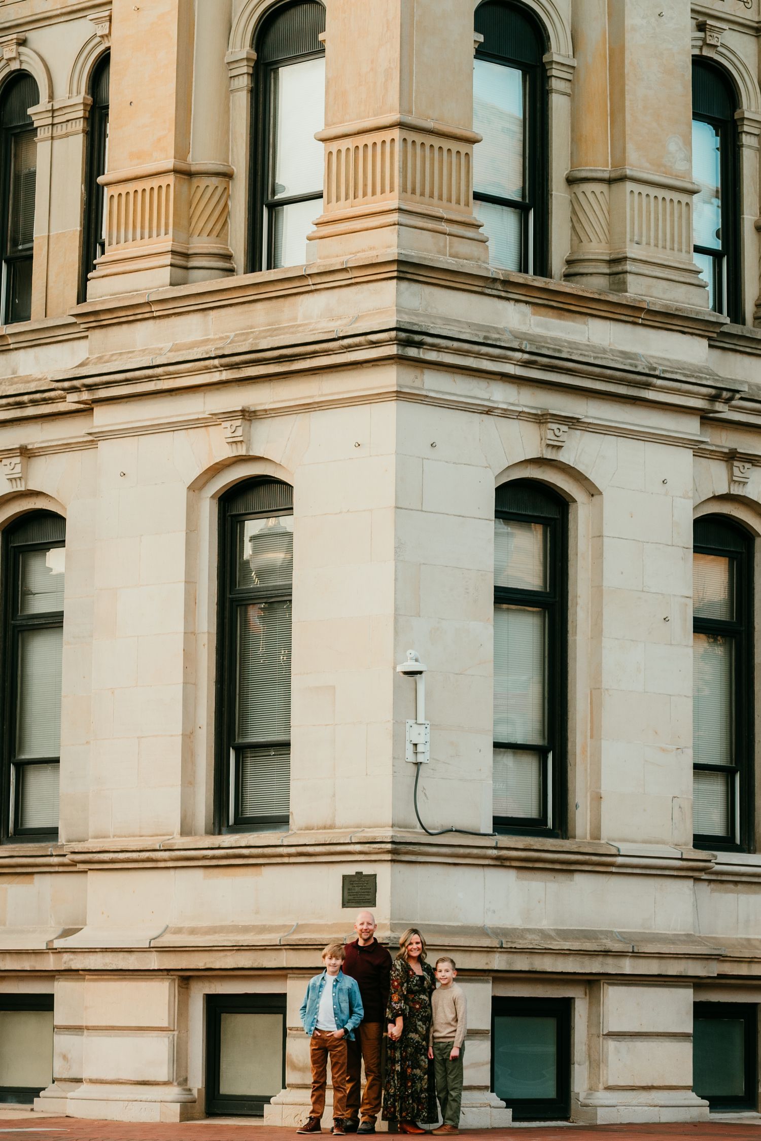 Family of four posing in front of a grand historic stone building corner facade.