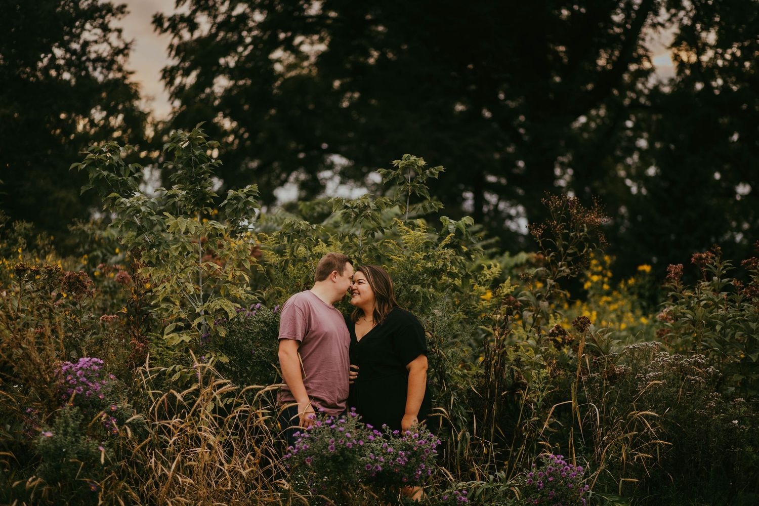 Couple sharing a tender moment surrounded by wildflowers in a lush garden at dusk.