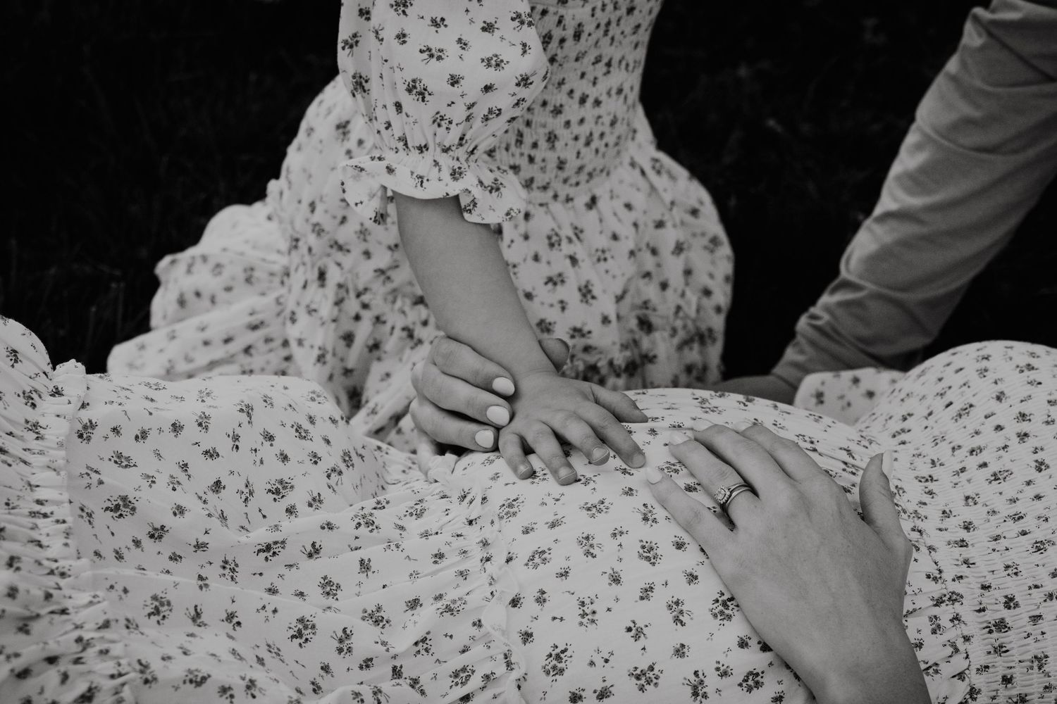 Black and white photo of hands touching a floral dress, capturing a tender moment.