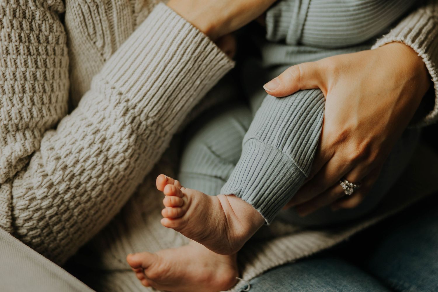Close-up of a parent cradling a newborn baby's tiny bare feet in their hands, wearing cozy knit sweaters.