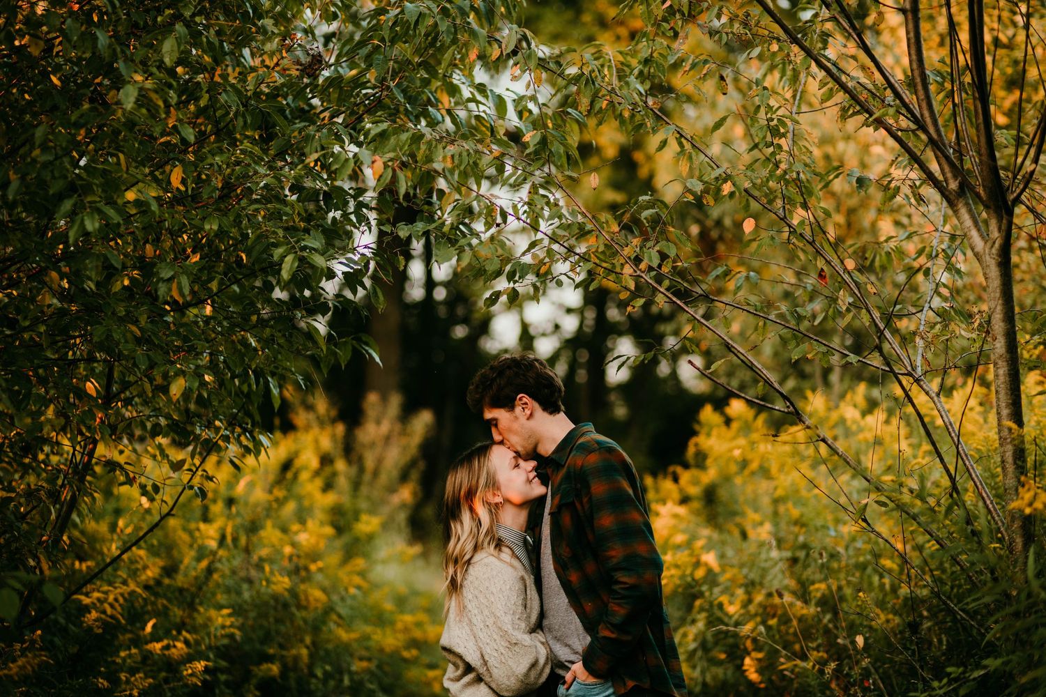 Couple sharing a romantic kiss surrounded by vibrant autumn foliage in the woods.
