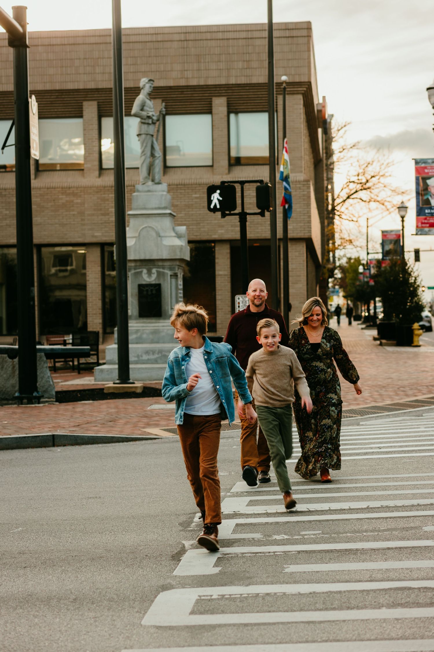 Family of four crossing a downtown street crosswalk near a historic statue and buildings.