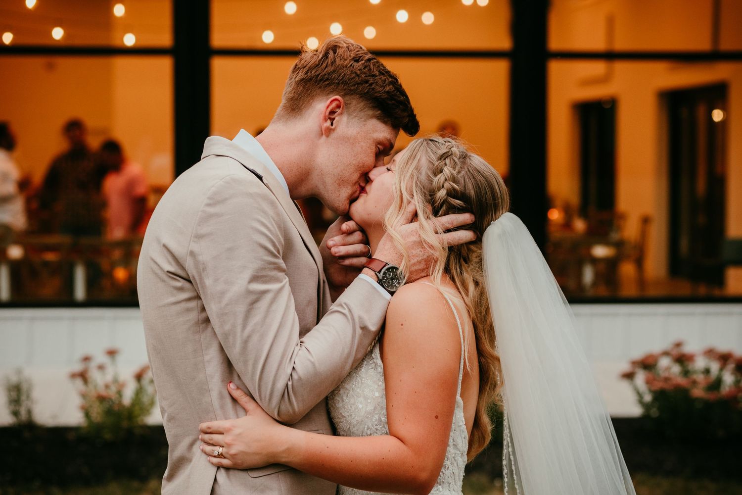 Bride and groom sharing a romantic kiss outdoors at their evening wedding reception.