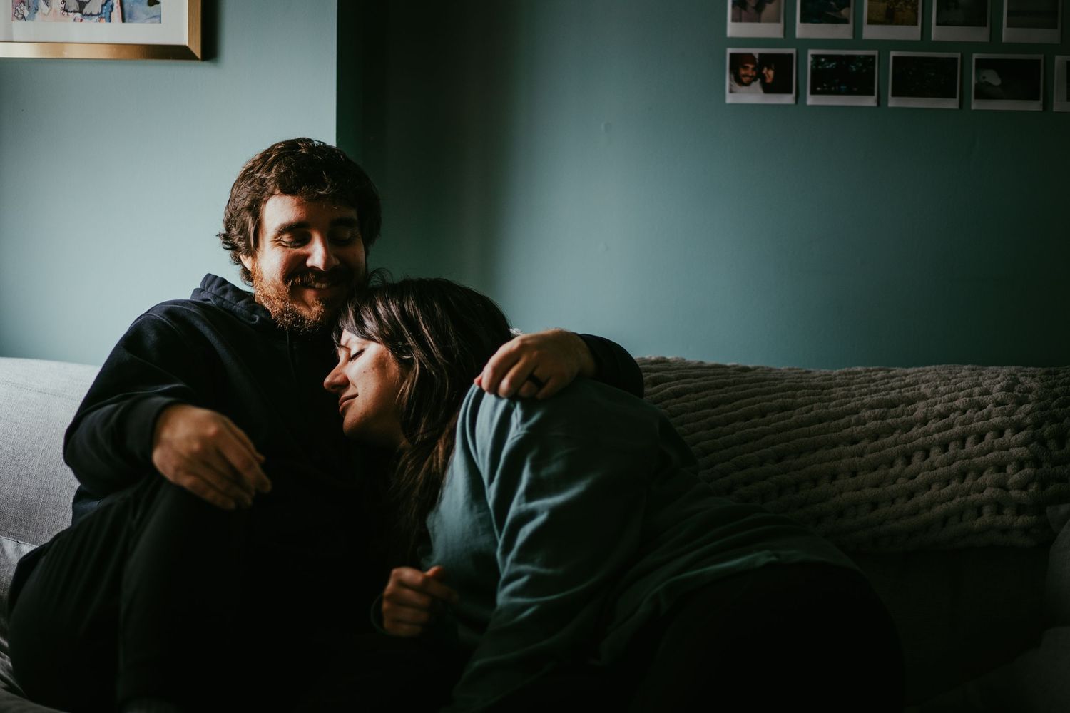 Couple cuddling together on a couch in a cozy dimly lit living room setting.