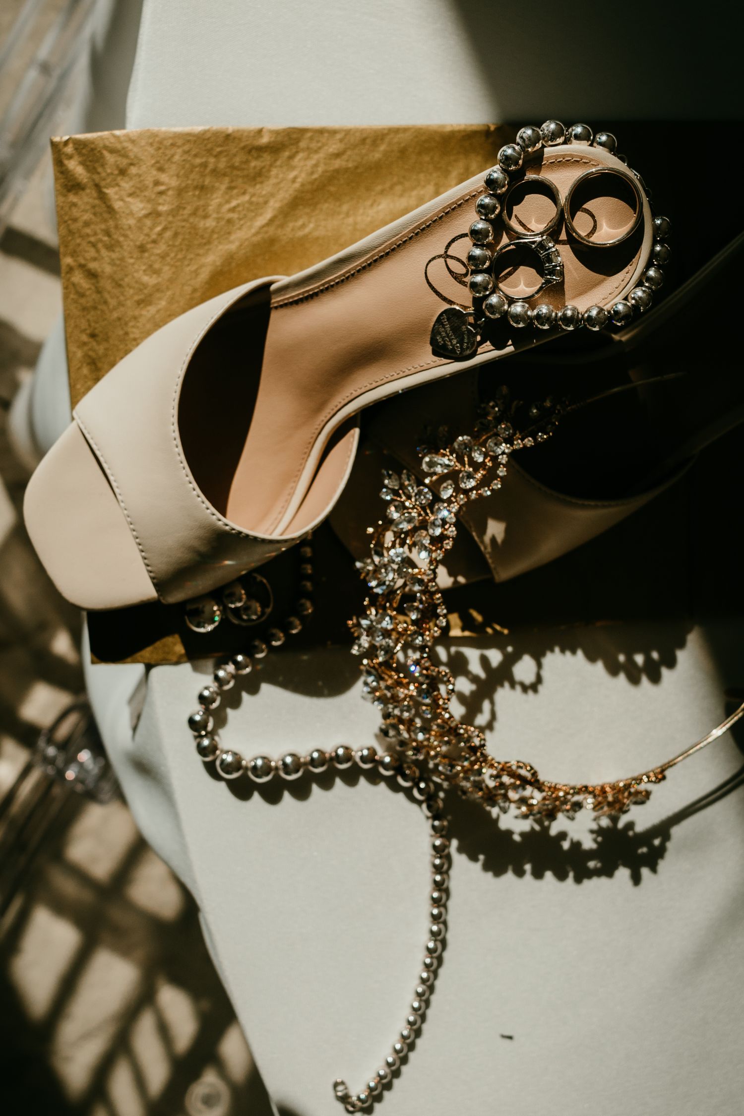 Beige bridal heels with pearl jewelry and gold necklace arranged on a golden envelope.